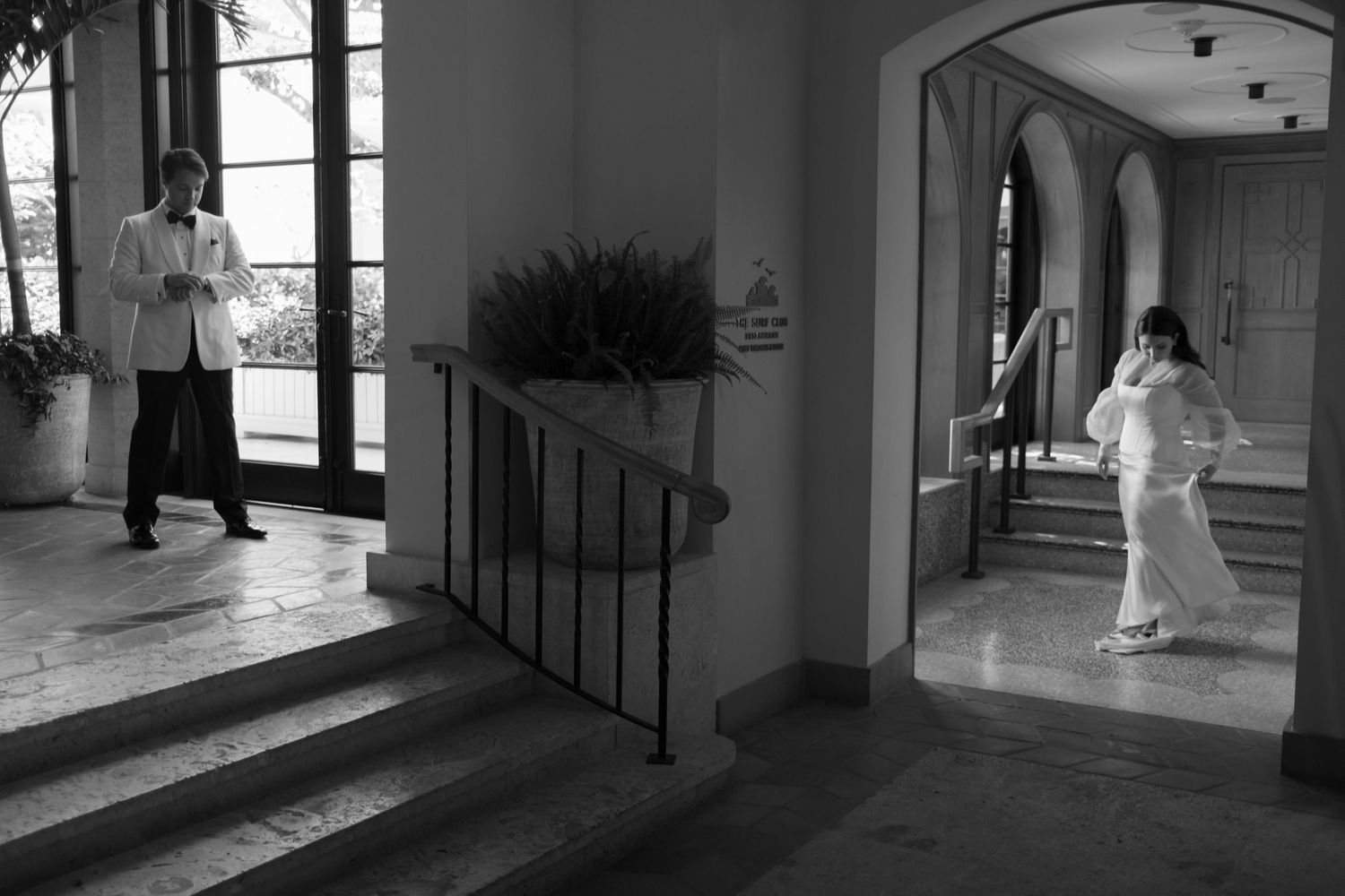 A black and white photo capturing a wedding moment in an elegant hallway with arched doorways.