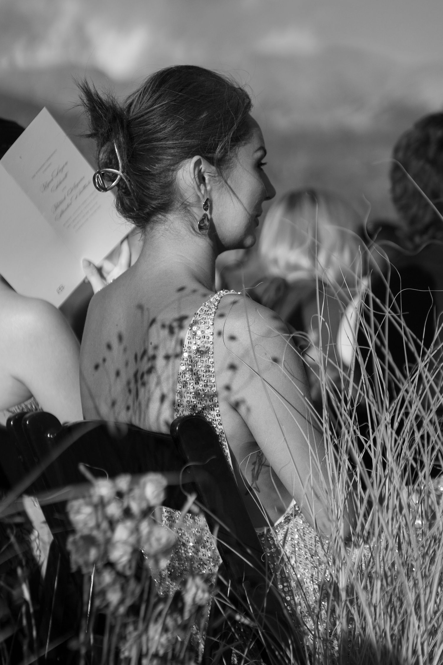 Black and white artistic portrait of a woman in tall grass wearing sparkly jewelry.