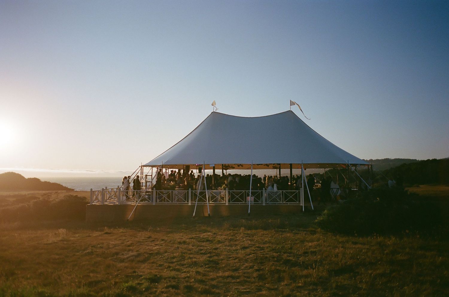 Large white wedding tent silhouetted against sunset sky in an outdoor venue setting.