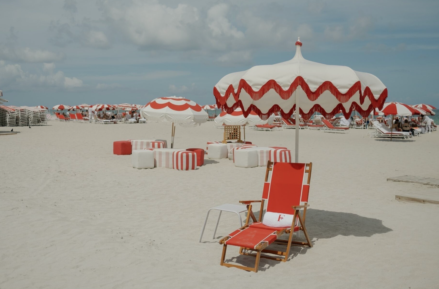 Beach scene with red and white striped umbrellas and lounge chairs on sandy shore.