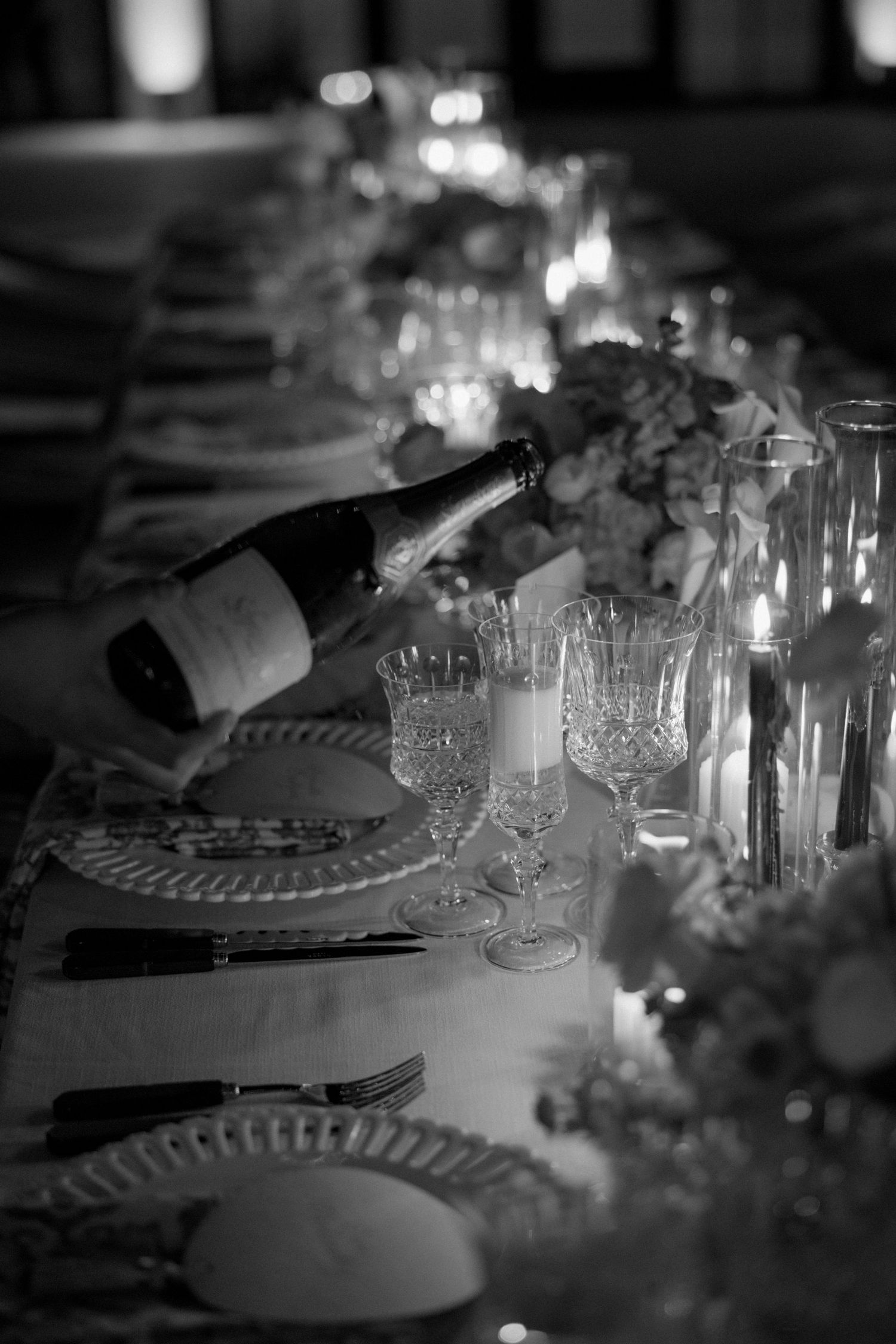 Elegant black and white table setting with crystal glassware and candlelight at a wedding reception.