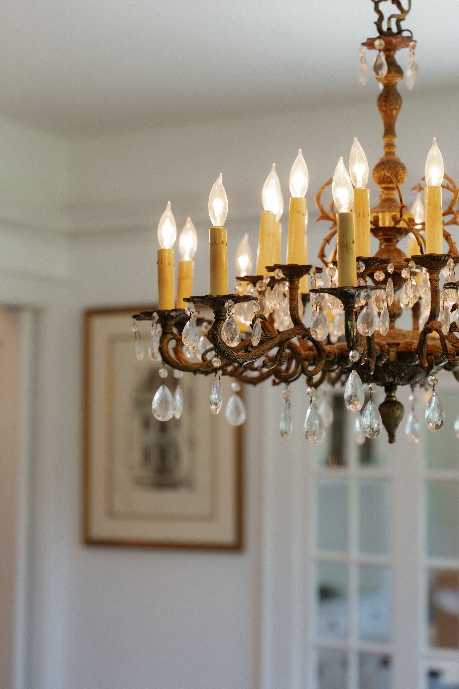 Elegant antique brass chandelier with crystal drops and candle-style lights illuminating a bright wedding venue.