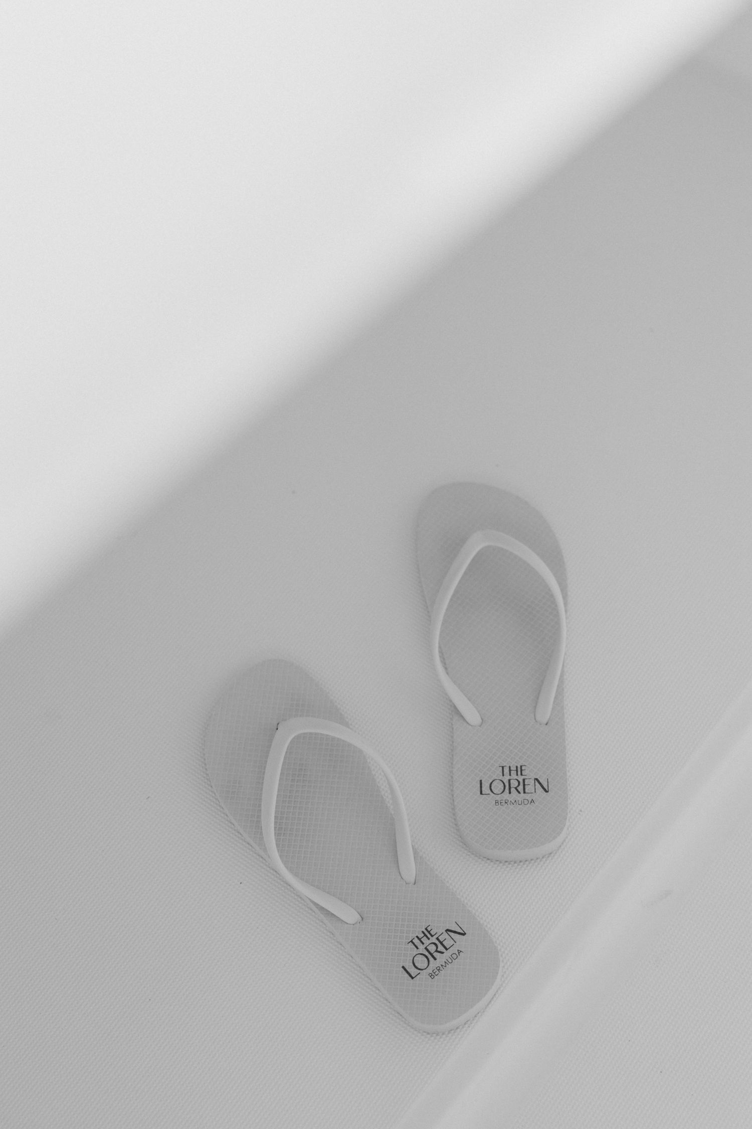 A pair of white sandals with the 'The Loren' logo on them.