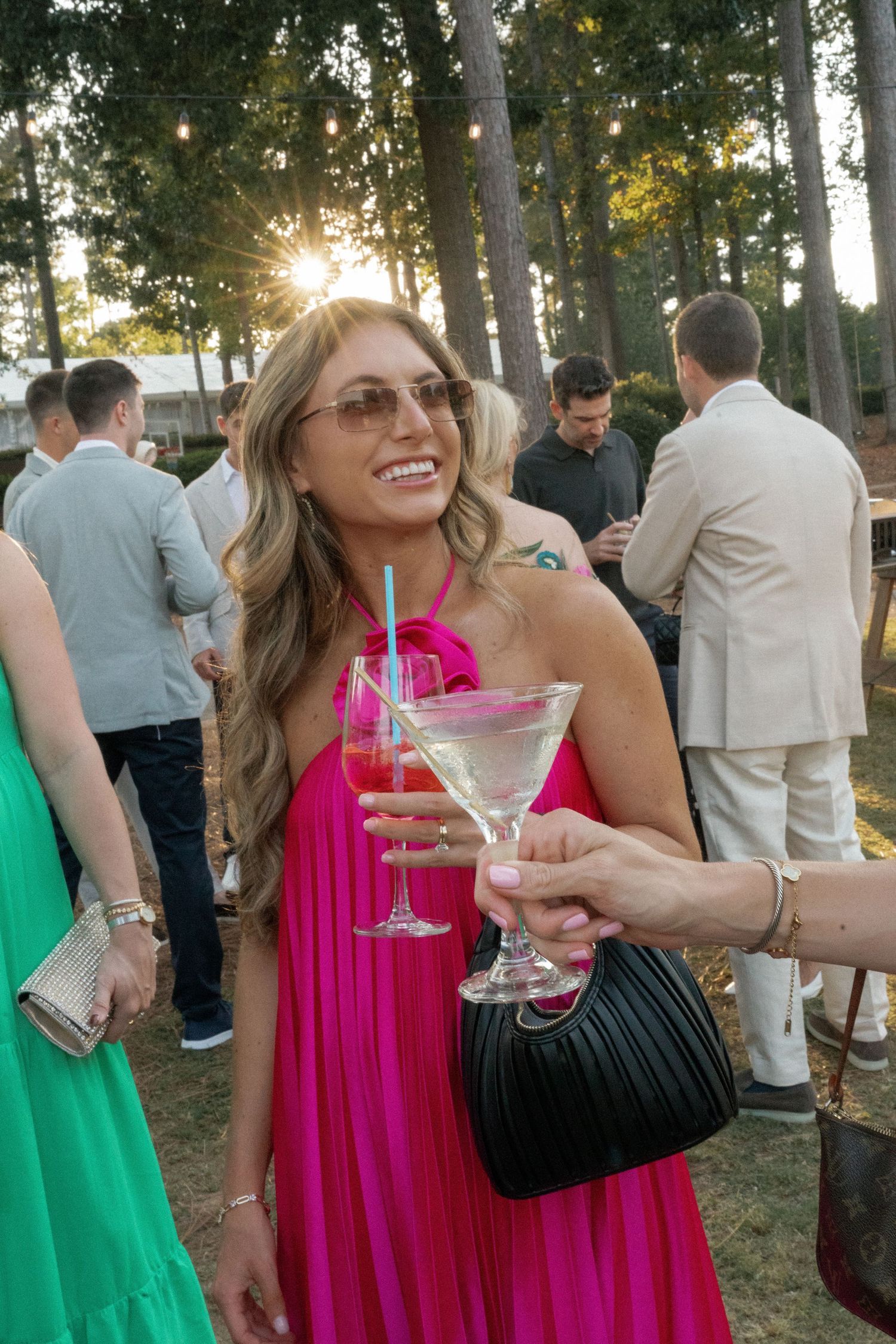 A guest in a bright pink dress enjoys cocktails at an outdoor wedding reception.