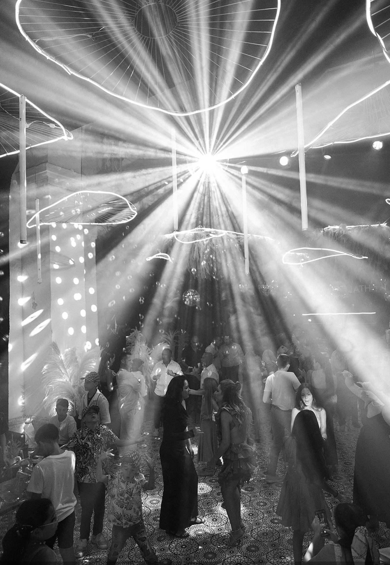 Dramatic beams of white light illuminate a dark nightclub filled with dancing silhouettes and atmospheric smoke.