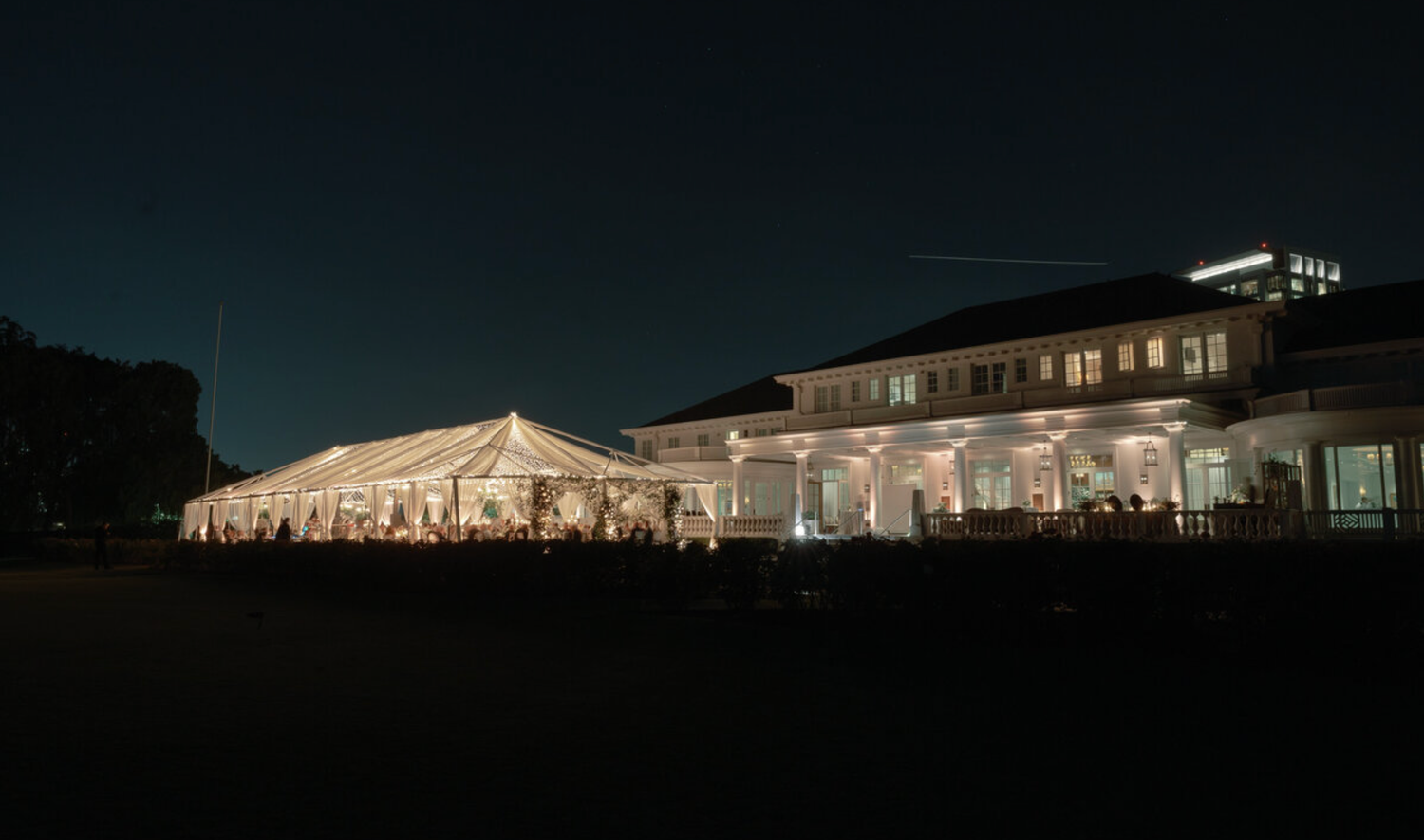 Illuminated white wedding tent venue glowing against a dark night sky.