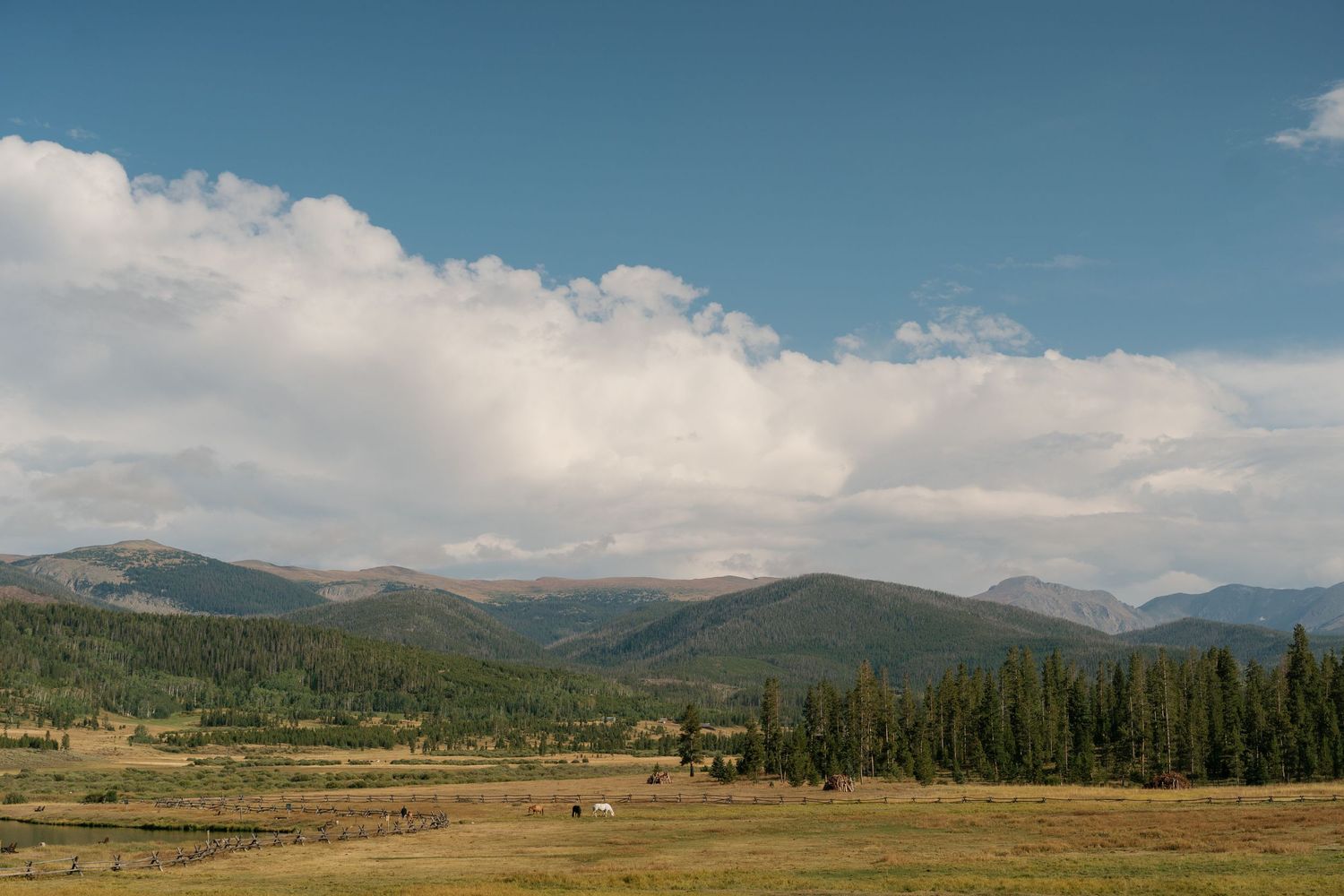 Panoramic mountain landscape with rolling hills and scattered clouds under blue sky.