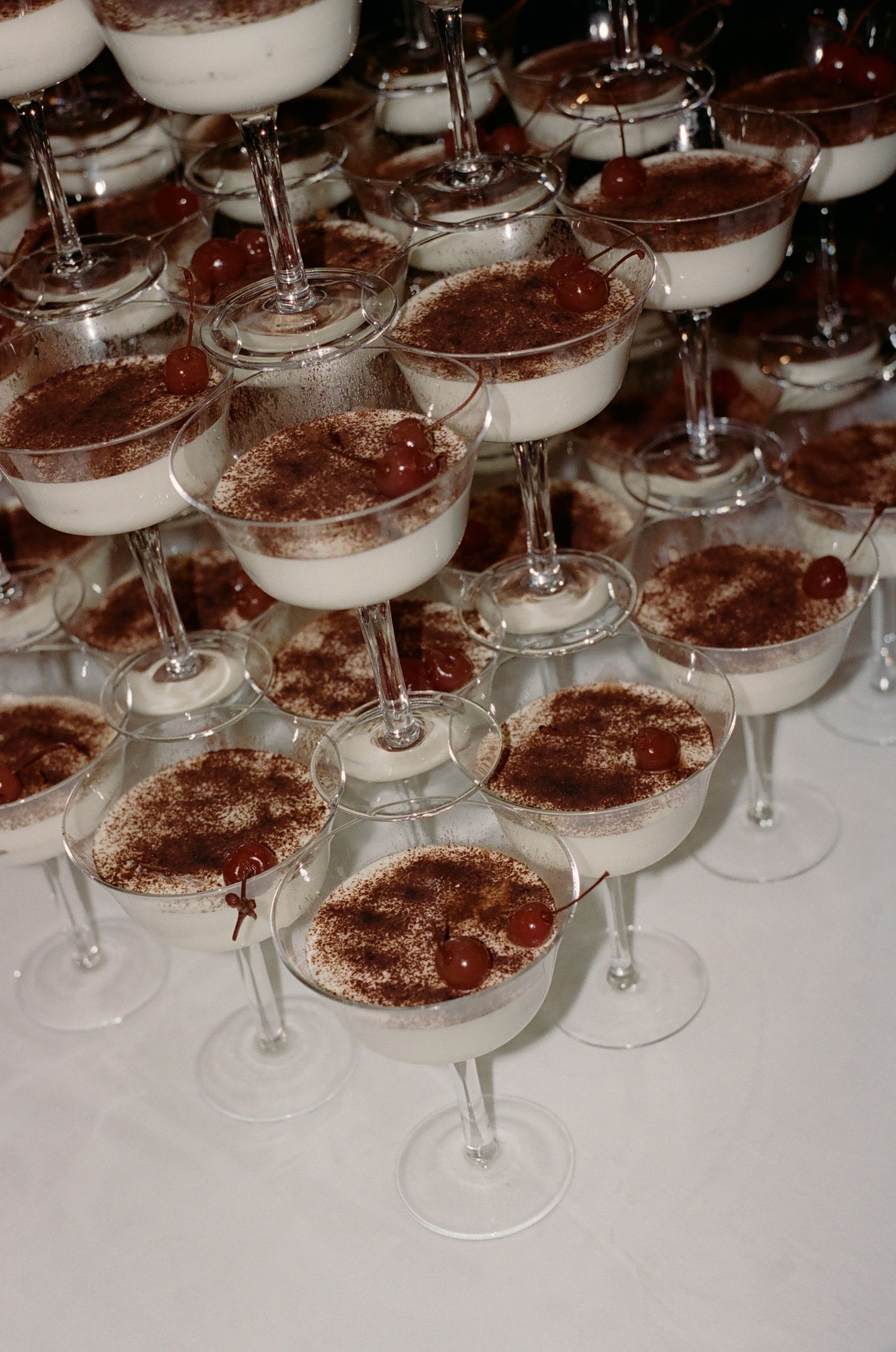 Multiple dessert glasses filled with tiramisu arranged in neat rows on a white surface.