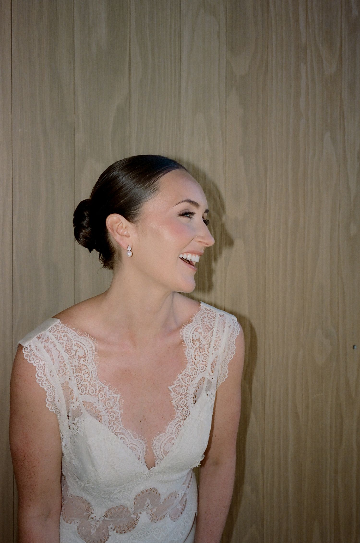 Close-up of delicate white lace detail on wedding dress against wood paneled wall.