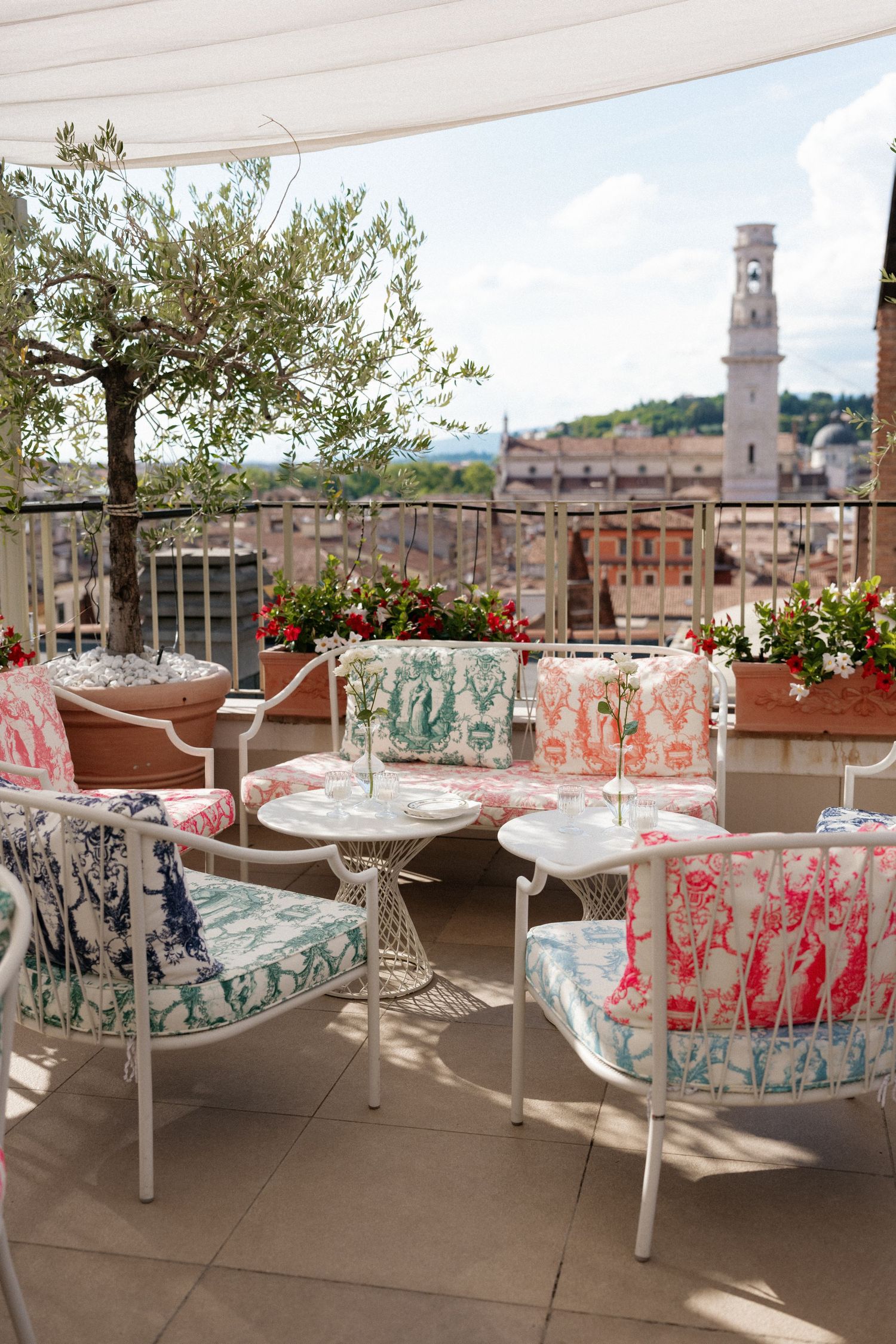 Elegant rooftop terrace with colorful patterned chairs and tables overlooking Verona cityscape and bell tower.