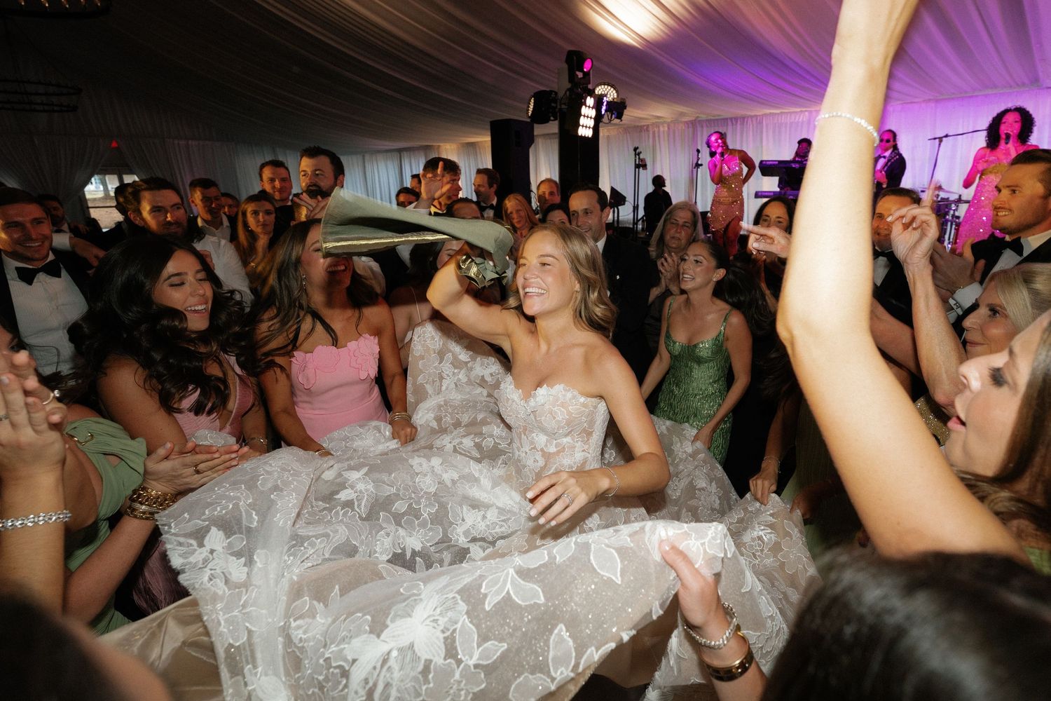 Energetic dance floor scene with guests celebrating around a flowing wedding dress.