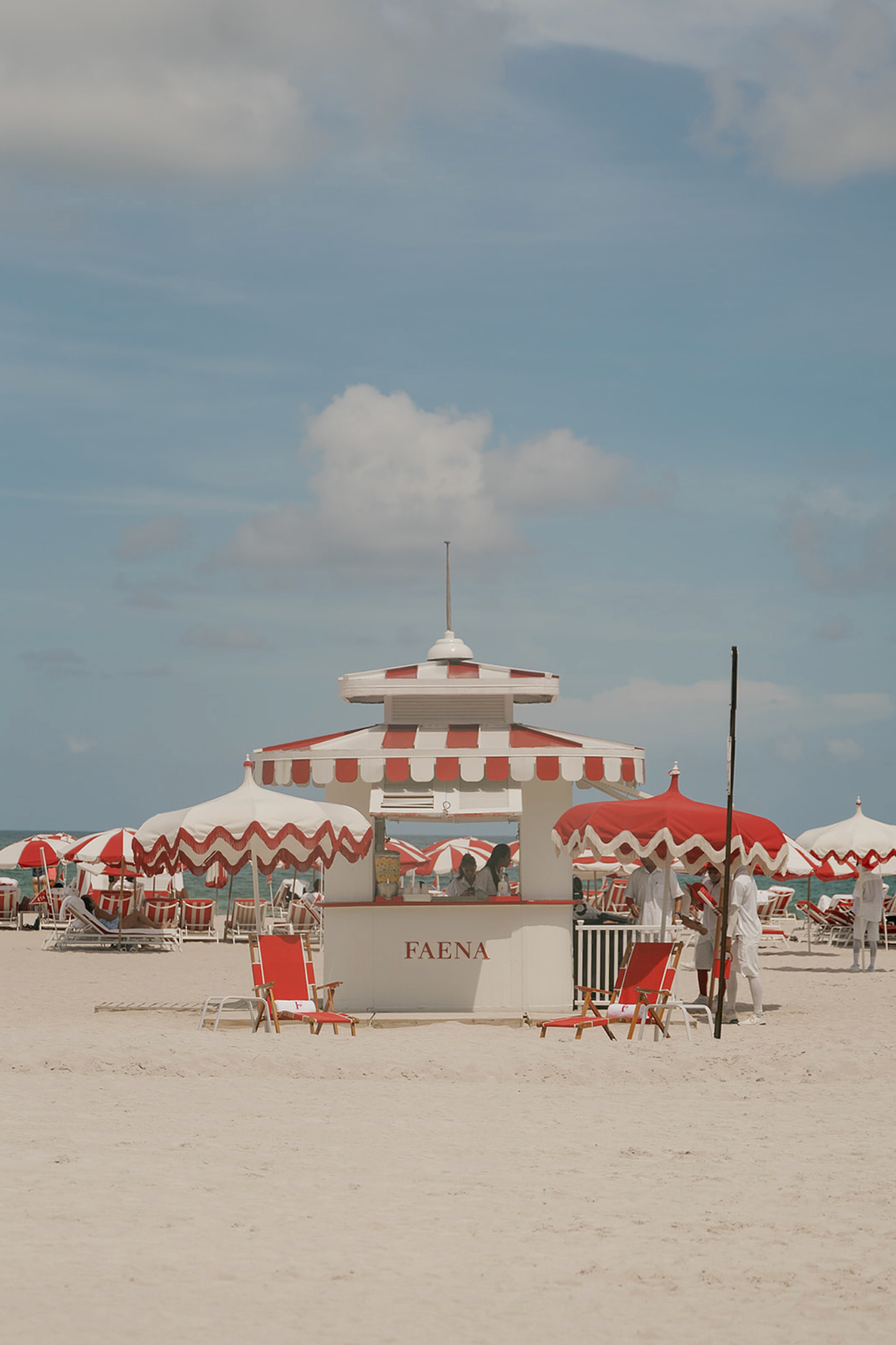 Red and white striped beach cabanas line a pristine white sandy beach.