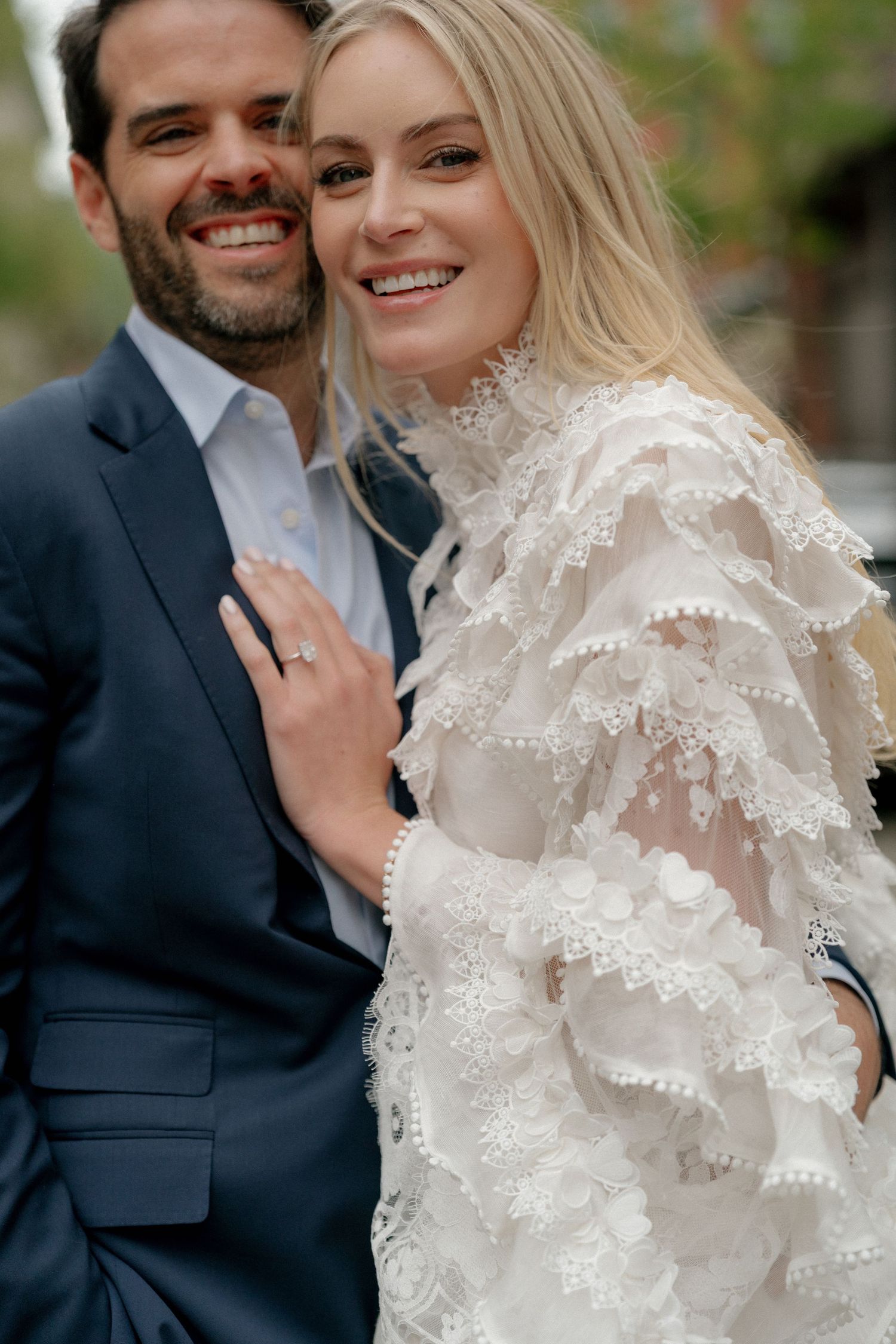 A couple in formal attire shares a tender moment against a natural backdrop.