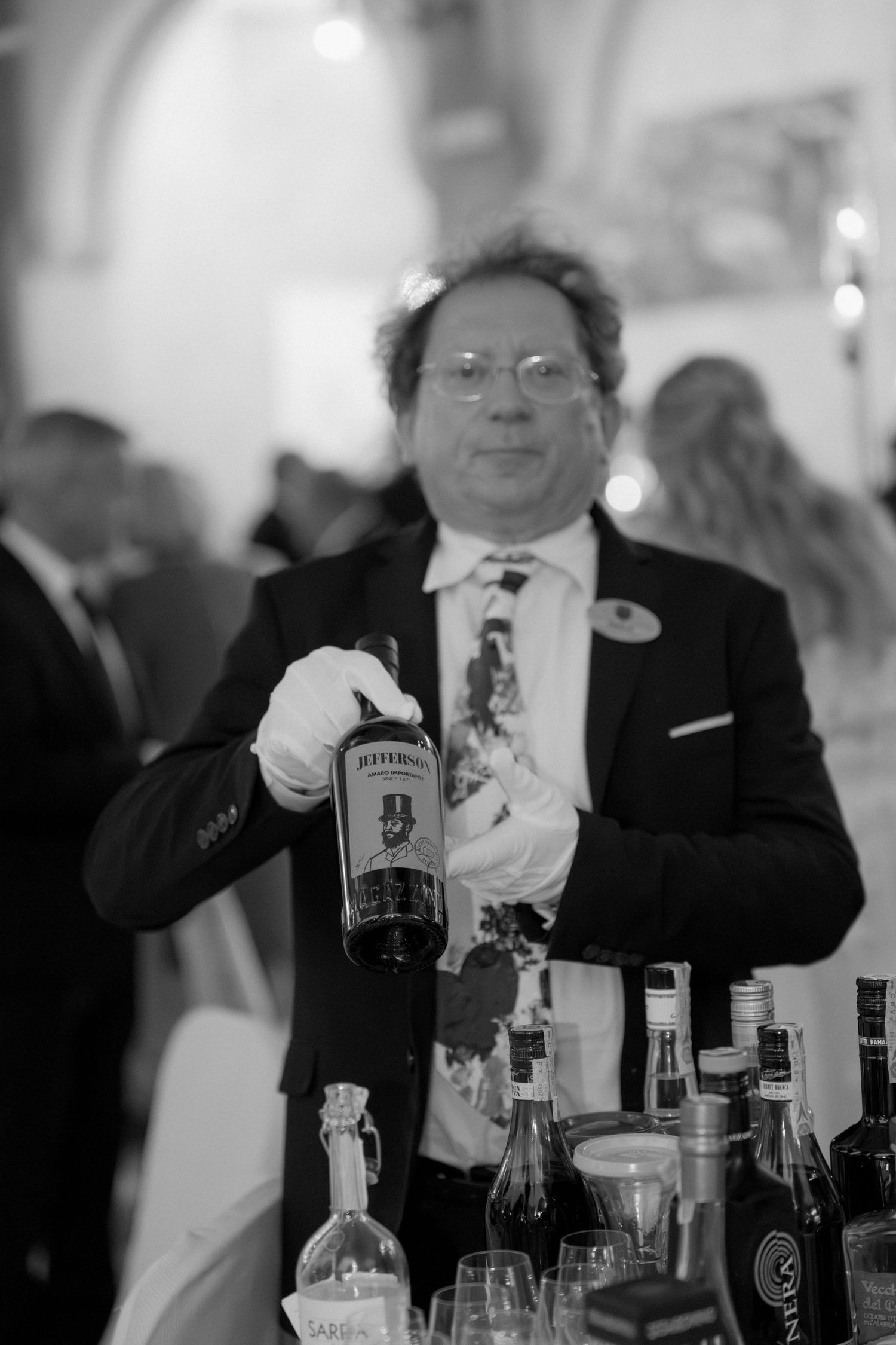 Bartender in tuxedo holding Jefferson's bourbon bottle at elegant black and white event bar.