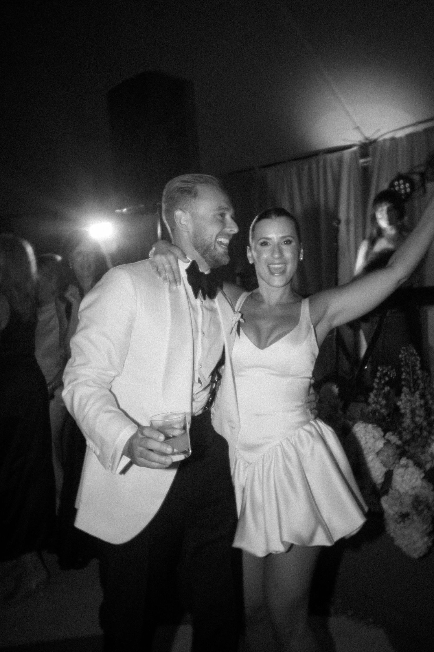 Wedding guests dancing energetically at a lively reception party in black and white.