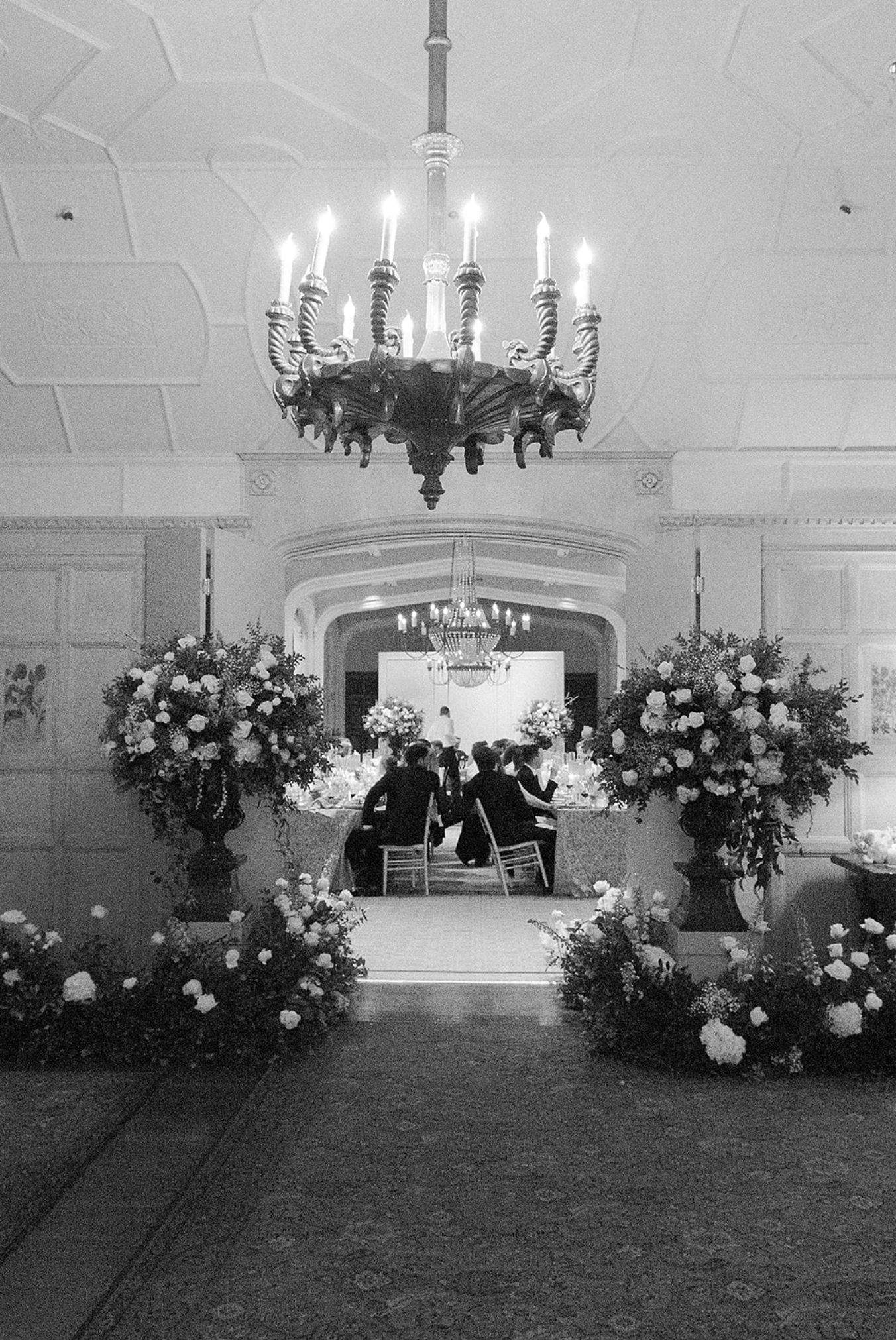 Elegant wedding venue interior decorated with white floral arrangements and chandeliers.