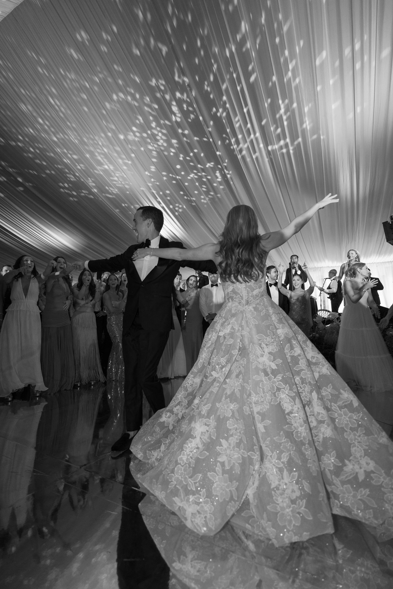 Dramatic black and white shot of wedding guests dancing under sparkling ceiling lights in a tent.