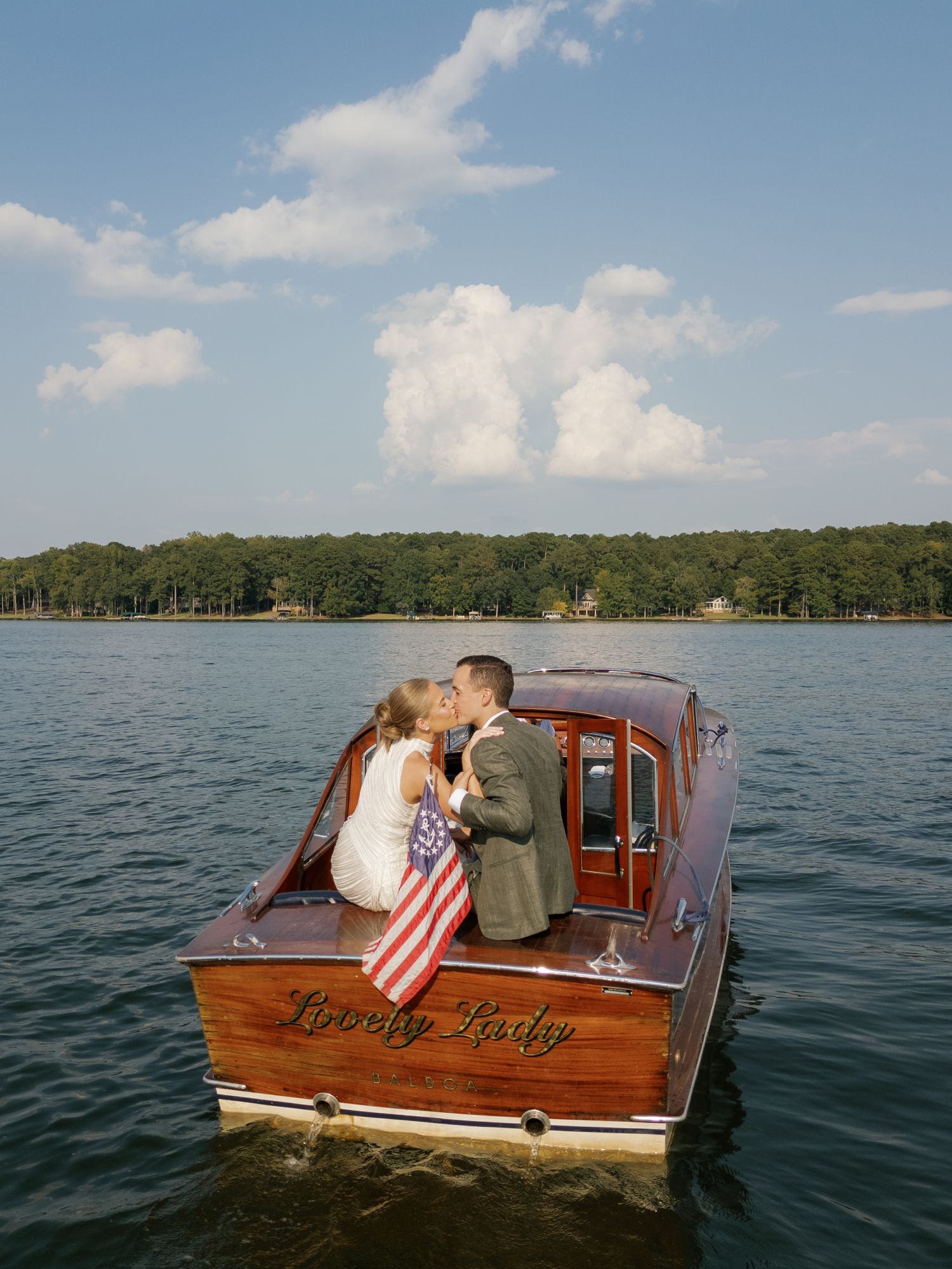 Classic wooden boat 'Evening Lady' cruising on a tranquil lake under blue skies.