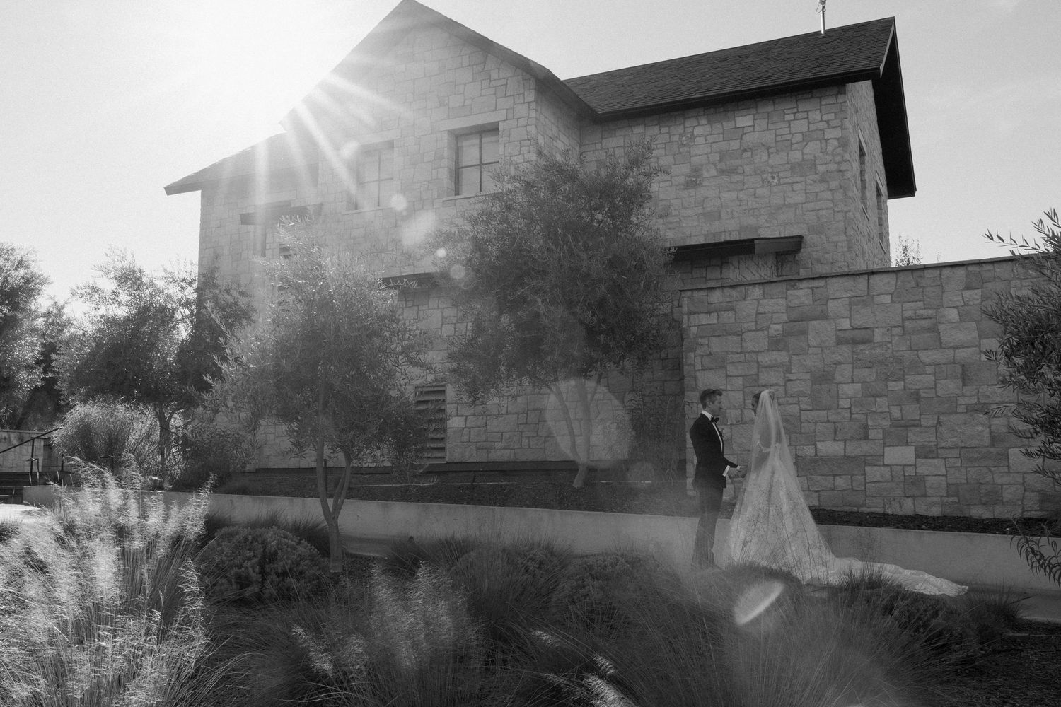 Black and white photo of a stone building with sunburst and wedding couple in silhouette.