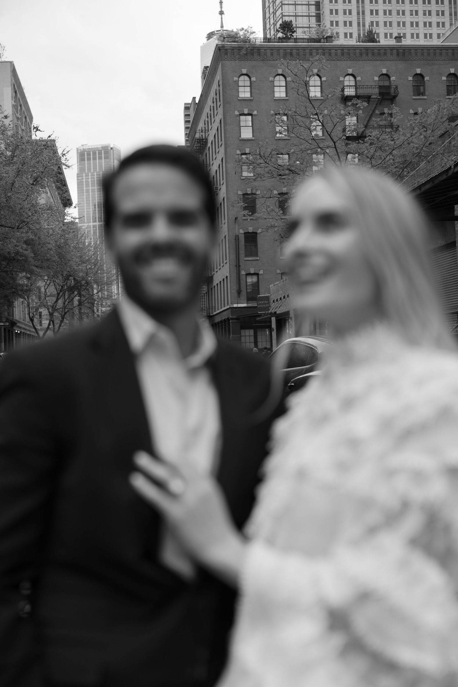 A black and white portrait of a couple against an urban cityscape.