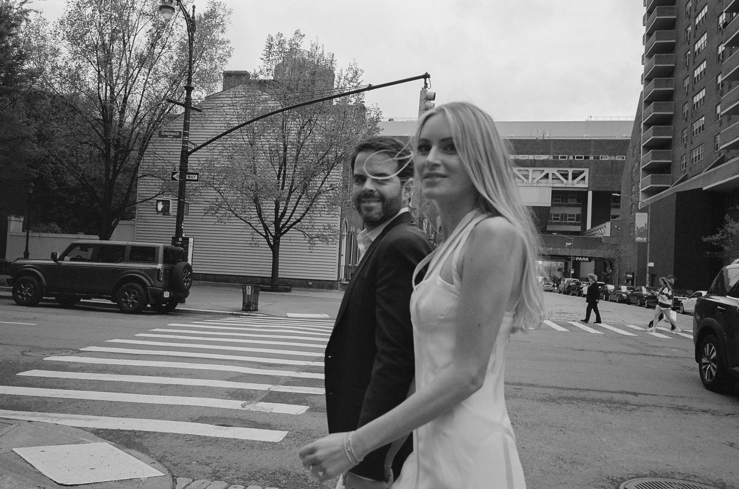 A couple walks together on a path near modern buildings and trees.