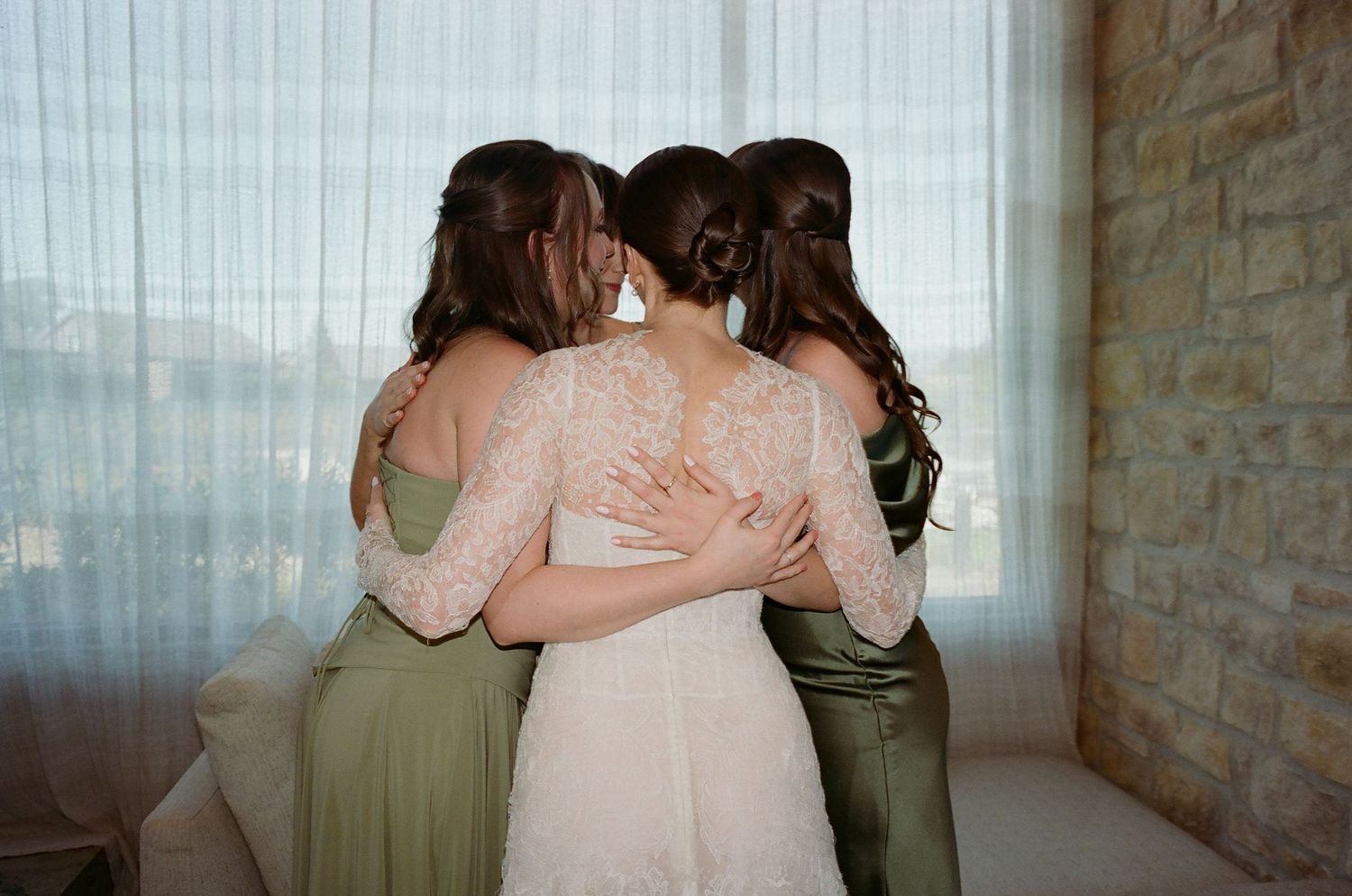 A bridal party shares an emotional moment in a room with stone walls and natural lighting.
