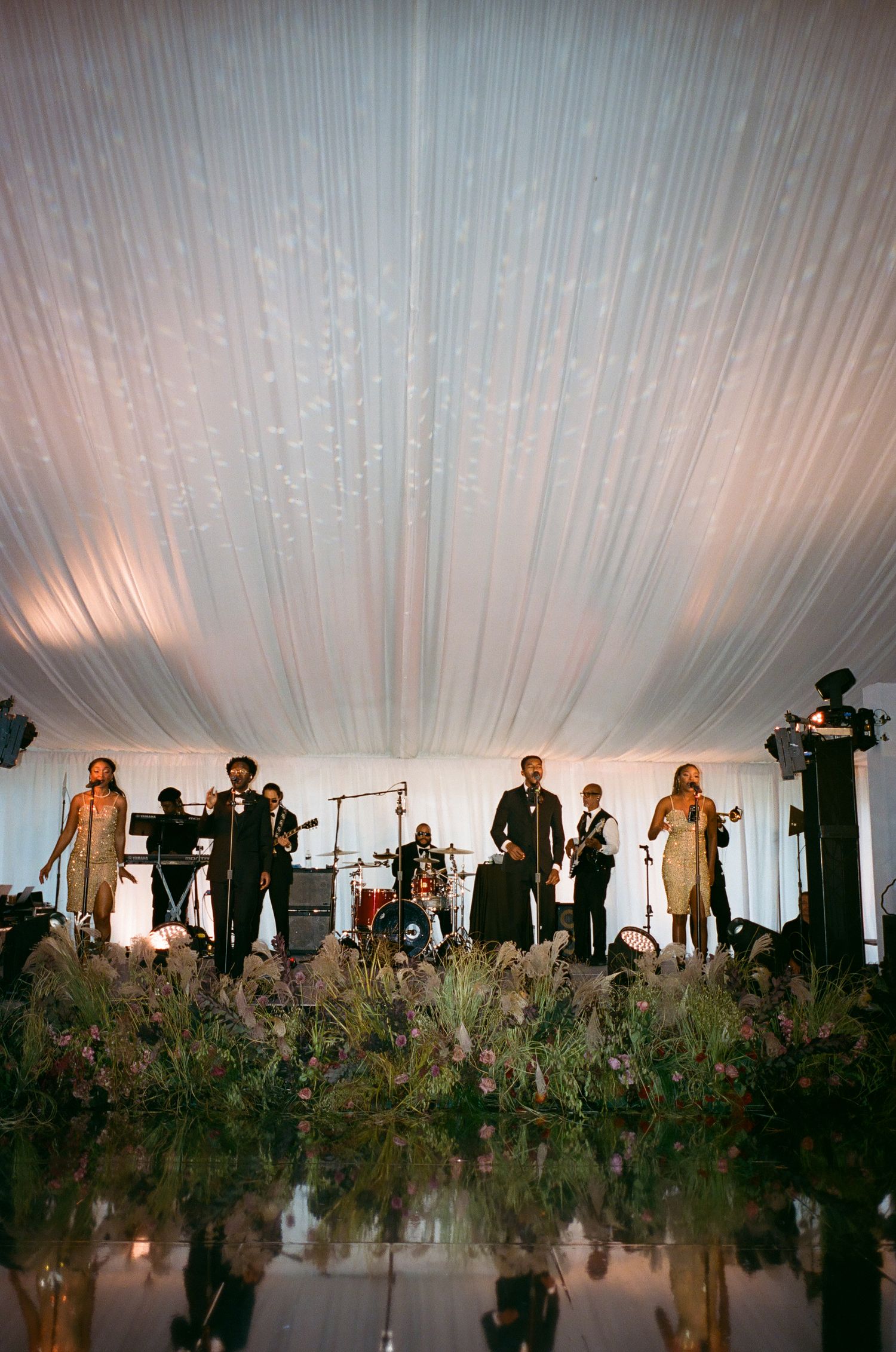 Wedding reception setup in an elegant white tent with floral decorations and band stage.