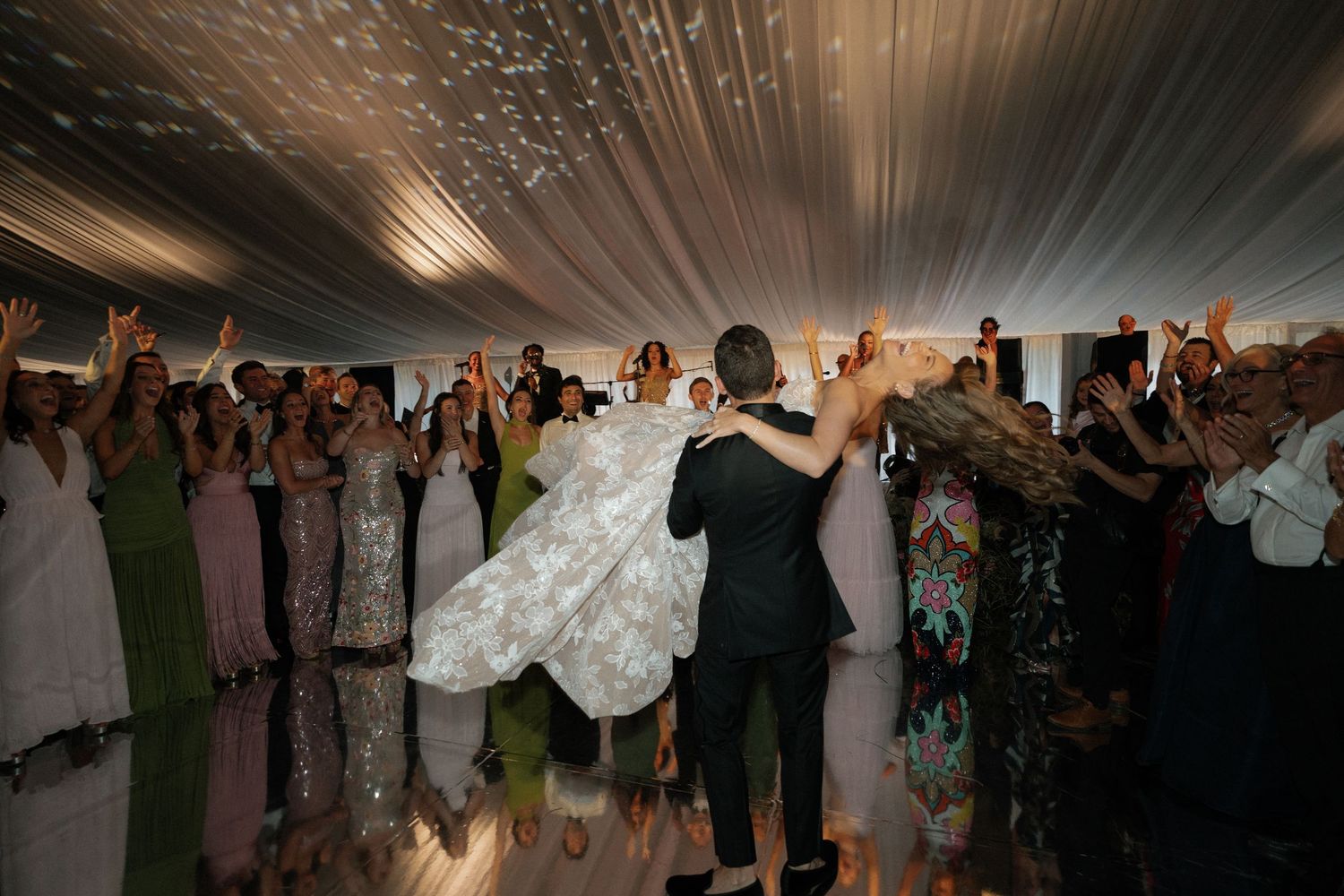 Energetic wedding celebration with guests dancing under a white tent with dramatic lighting.