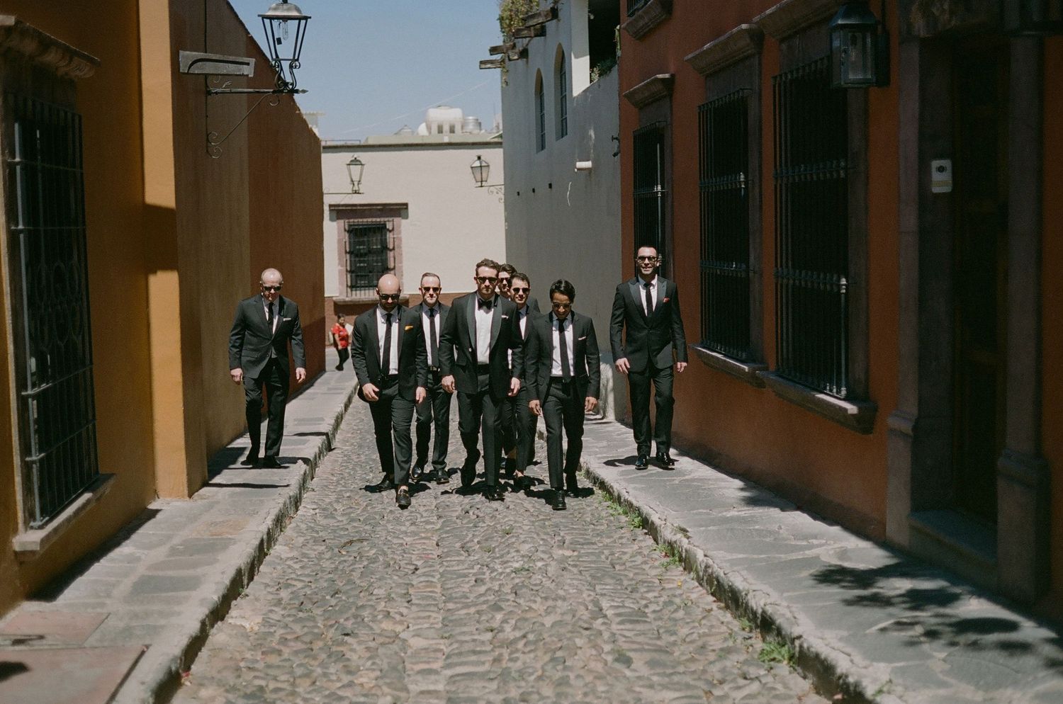 Group of men in dark suits walking down a narrow cobblestone street.