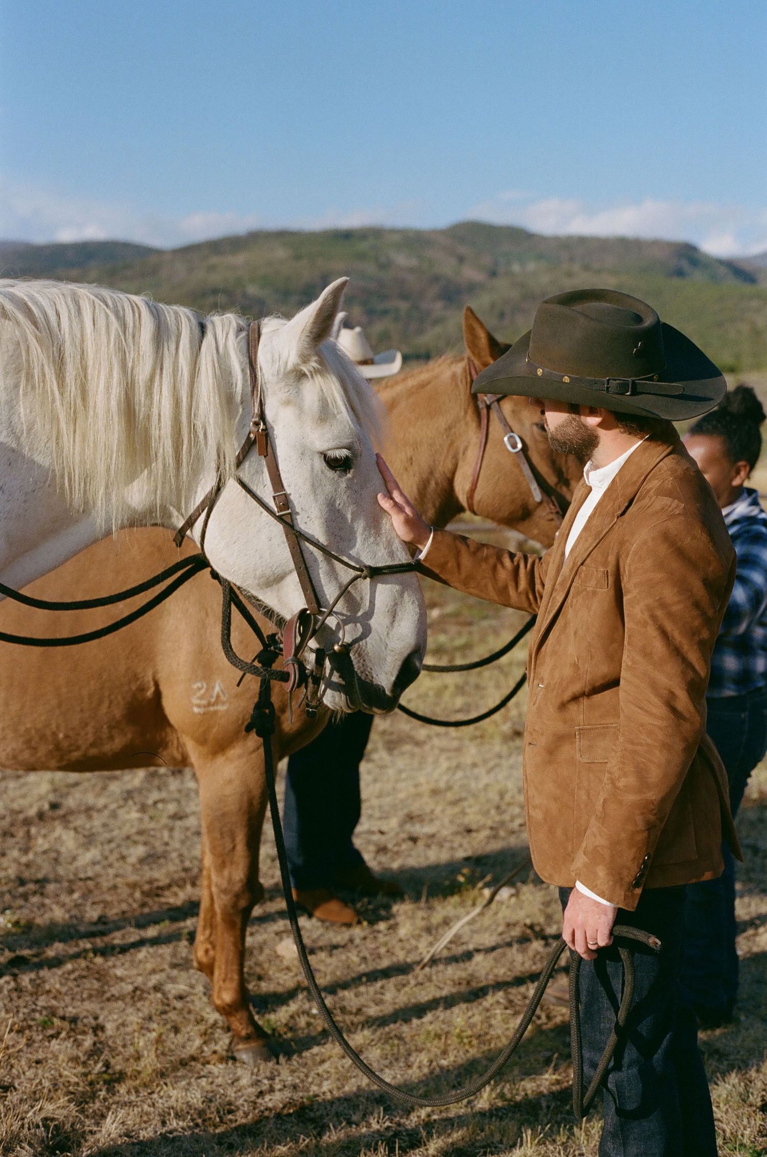 White horses with riders in western attire stand against a mountain backdrop.