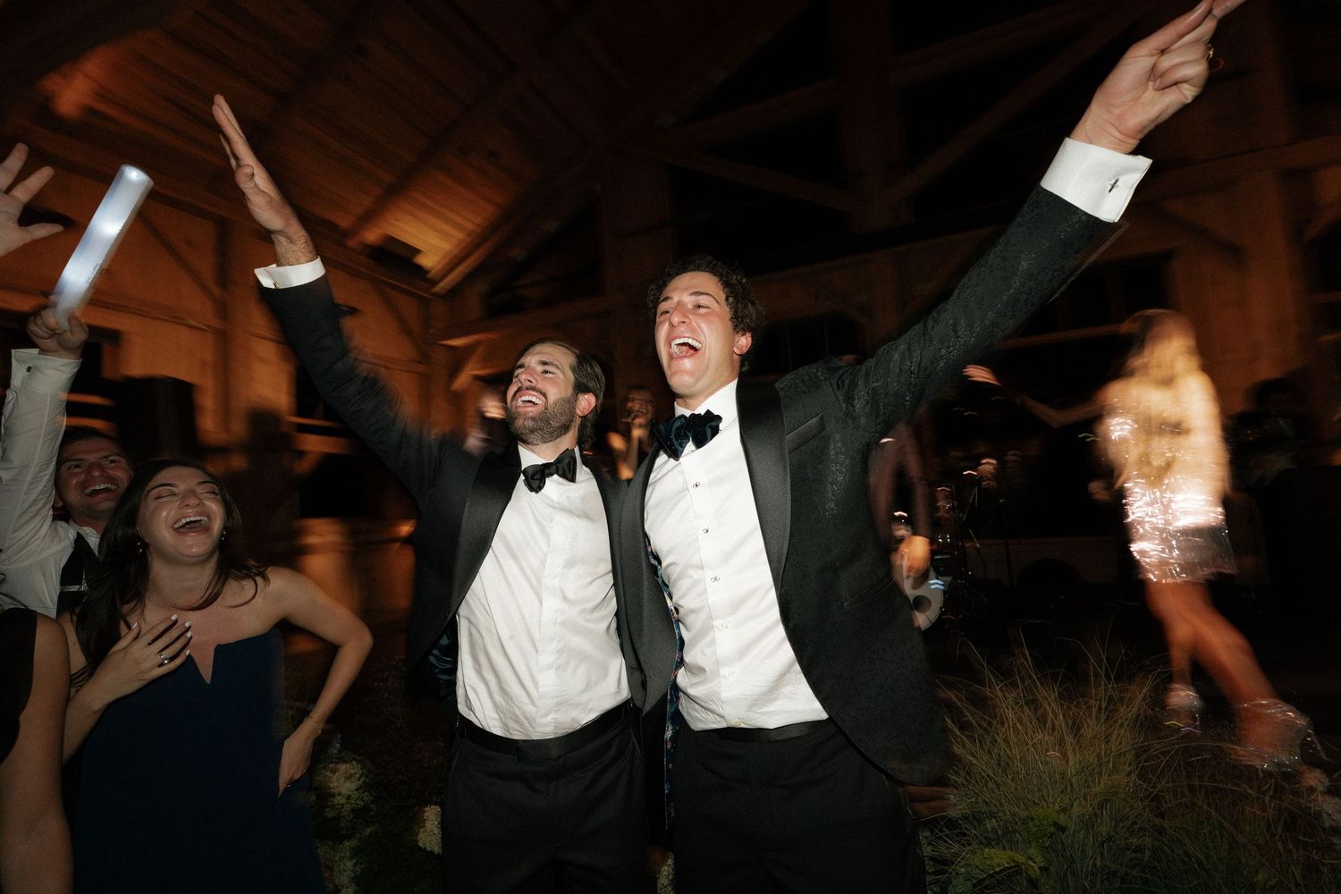 Wedding guests celebrate joyfully on a dance floor during an evening reception.