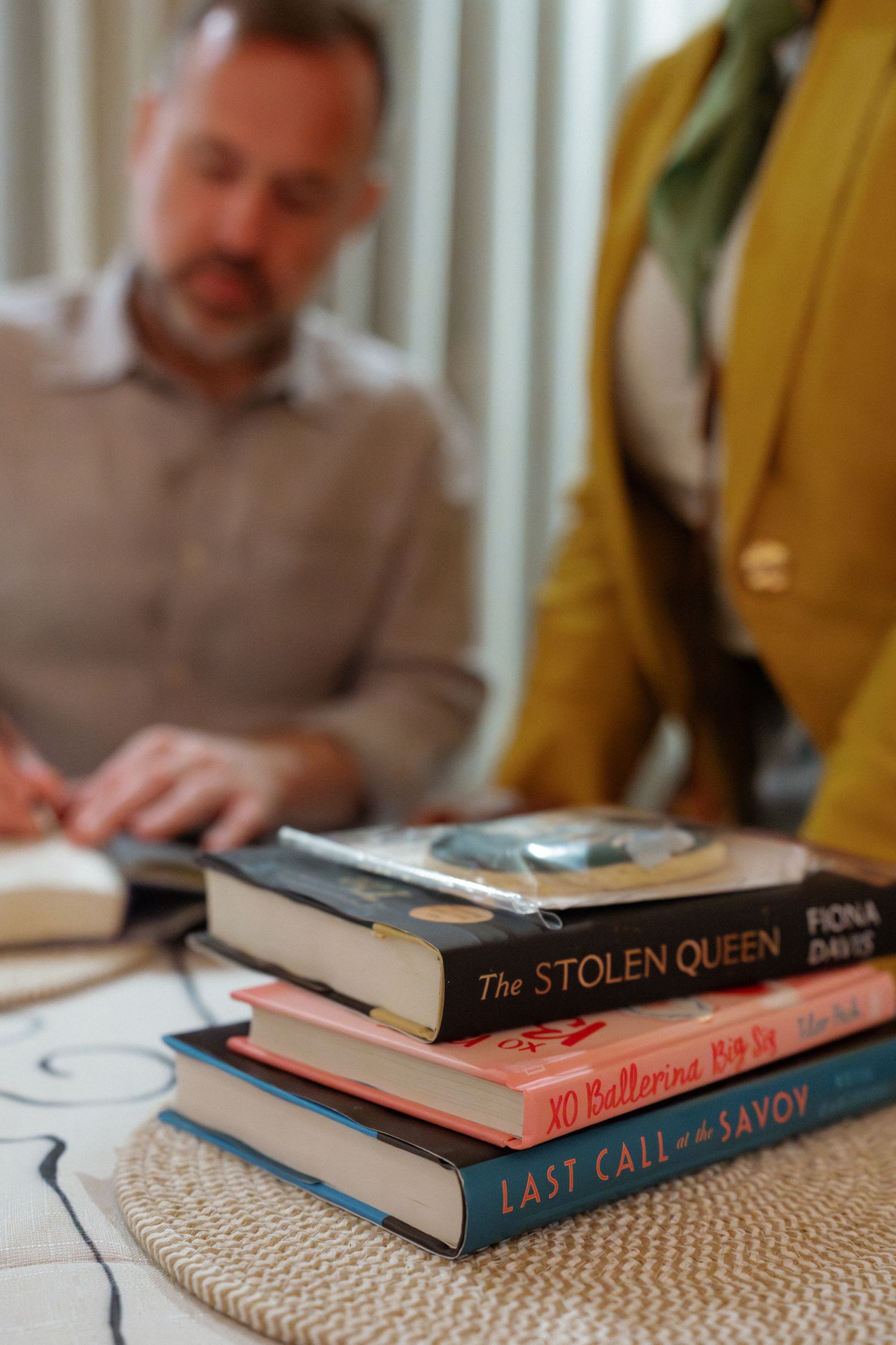 A stack of books, including 'The Stolen Queen' and 'Last Call at the Savoy', on a table.