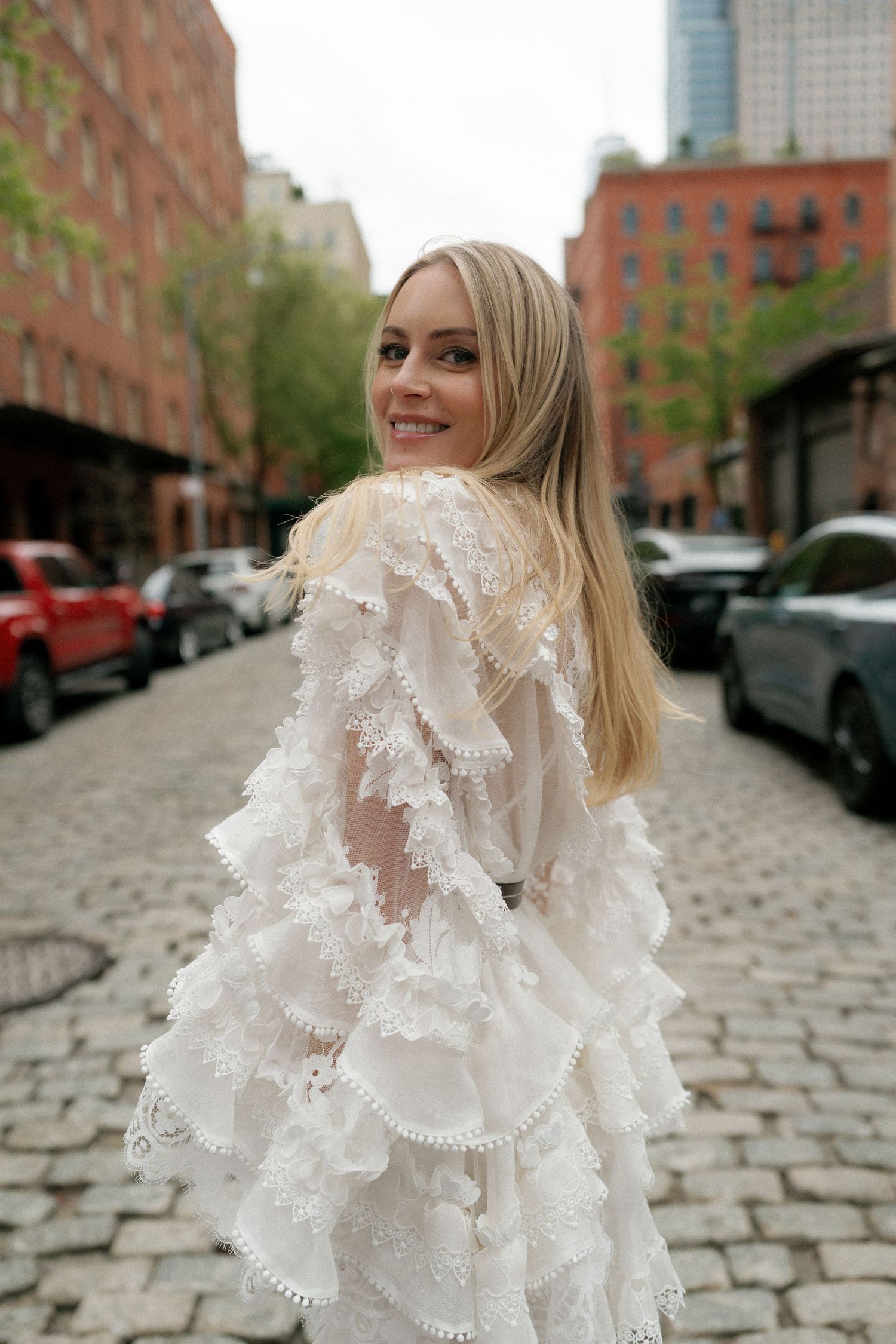 A person in an elegant white lace dress poses on a cobblestone street.