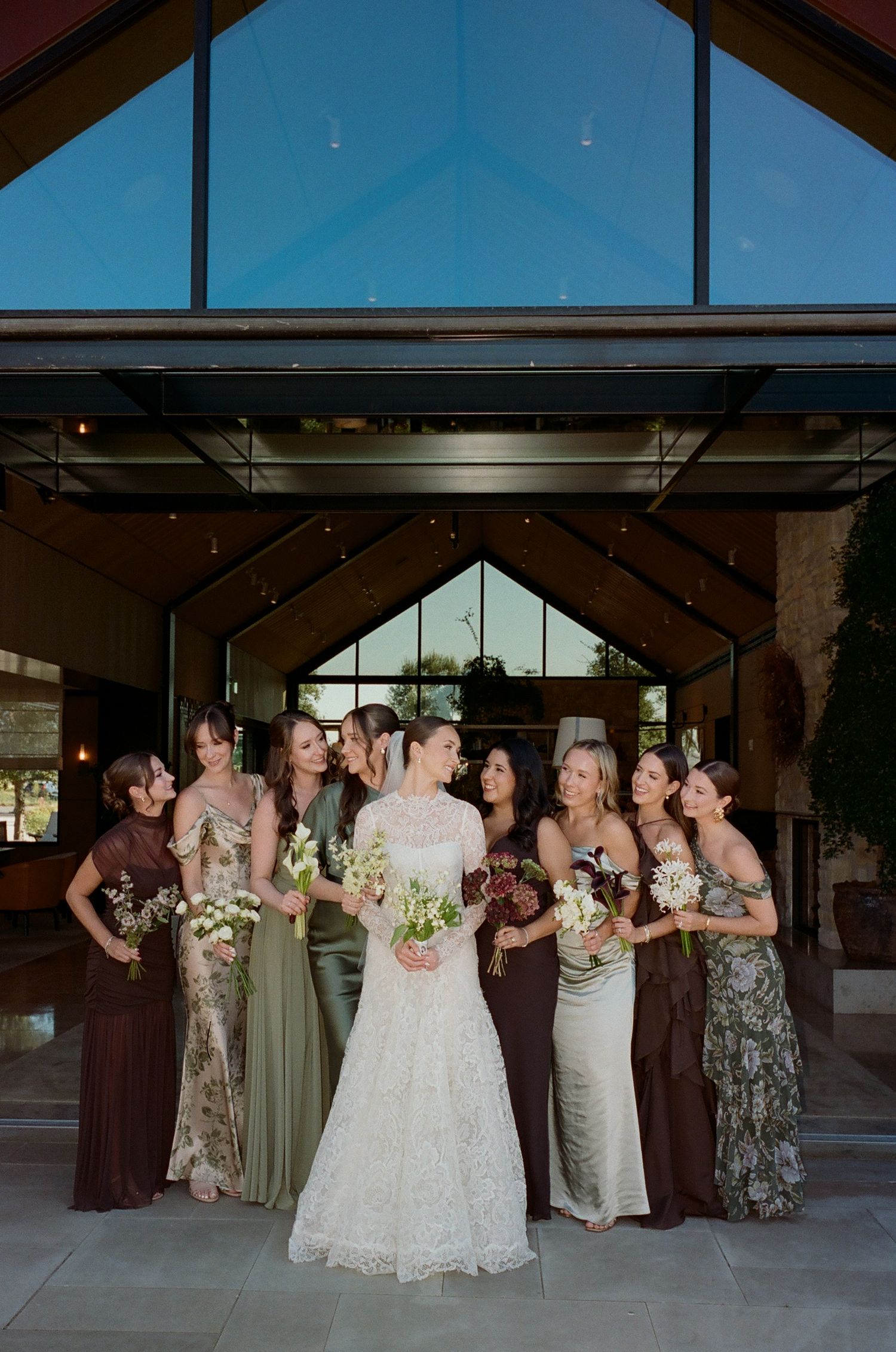 Wedding party poses together inside a modern venue with large windows and high ceilings.