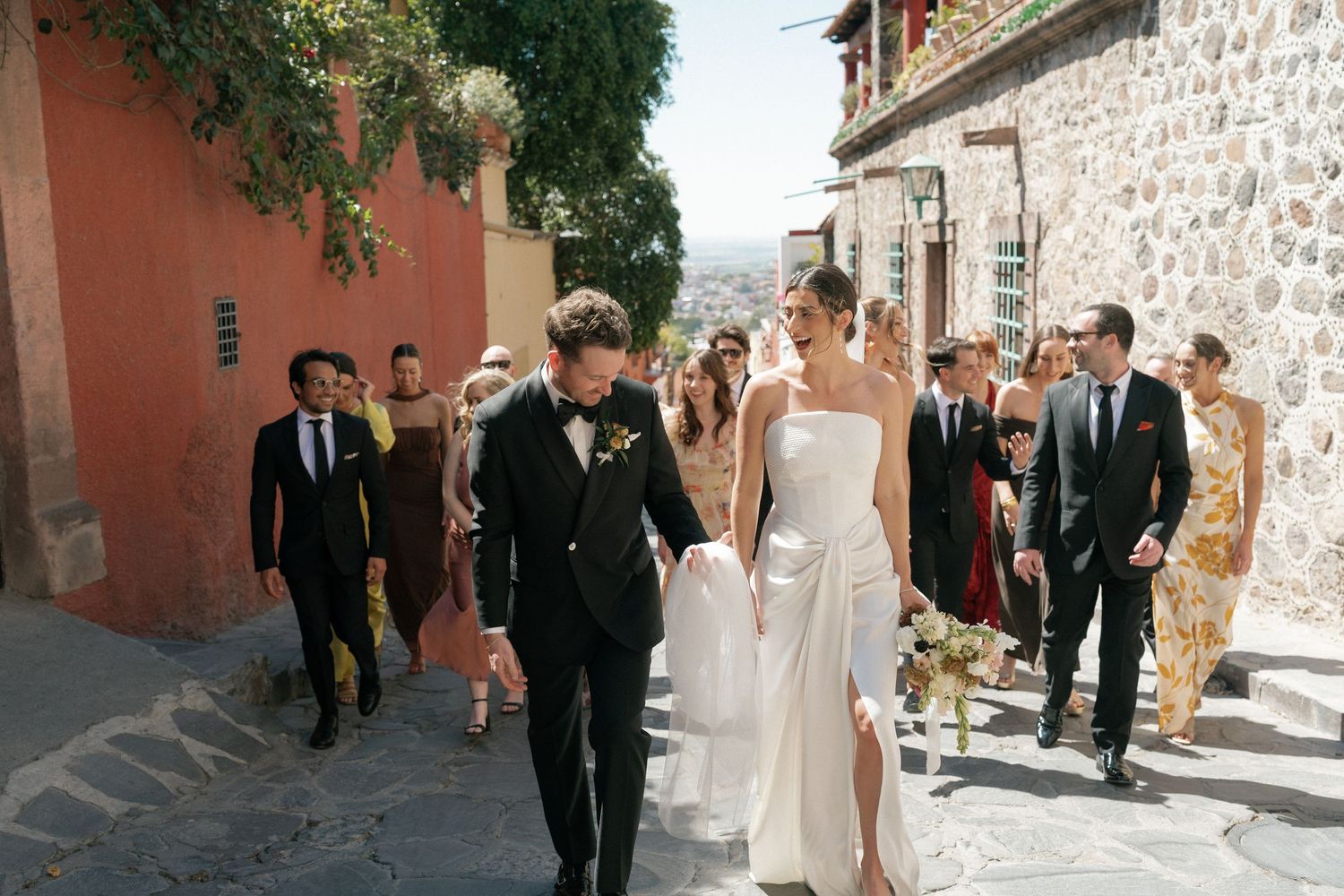 Wedding party walks down a charming cobblestone street in a European village setting.