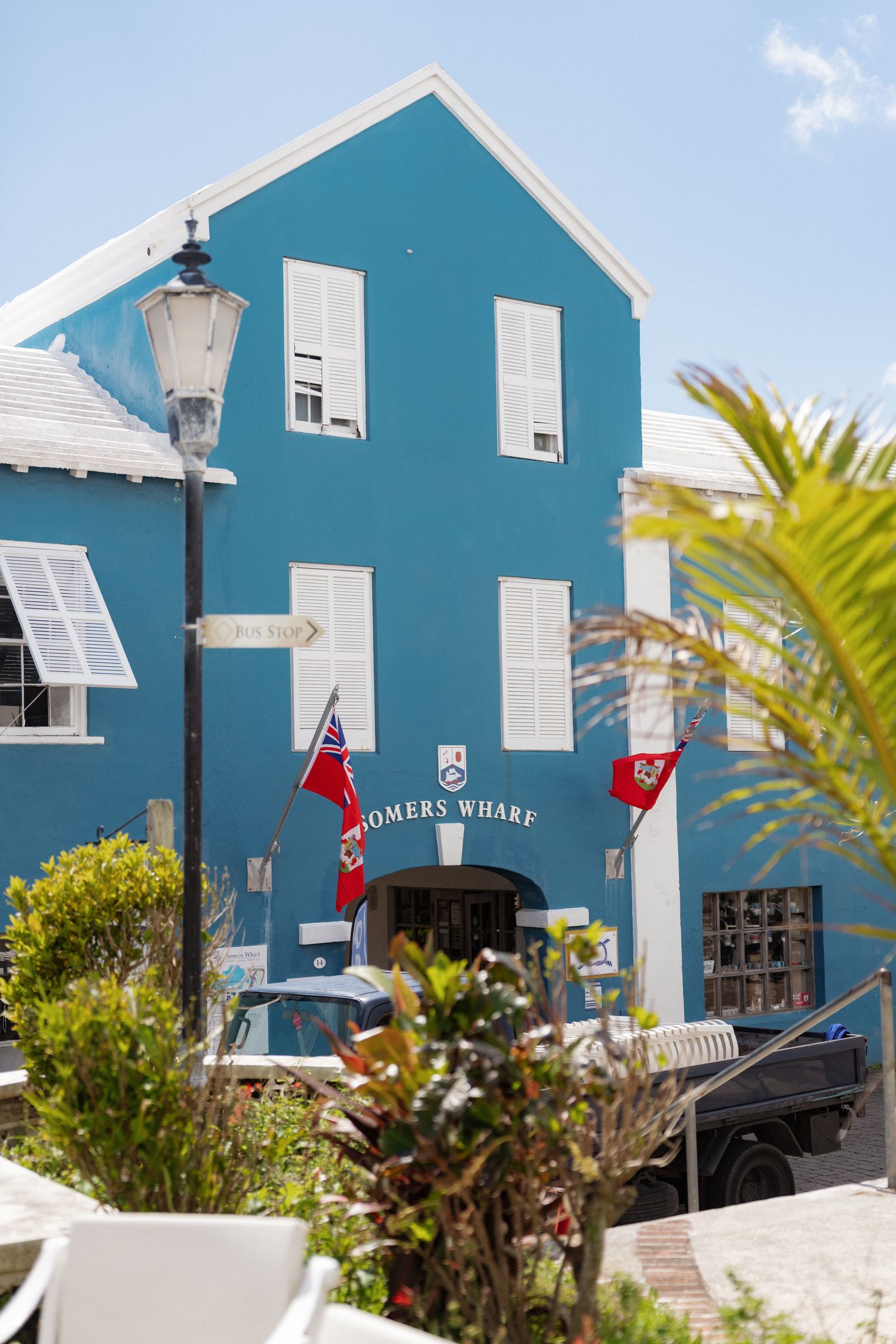 A brightly colored blue building with a red flag and lamp post in the foreground, surrounded by palm trees and greenery.