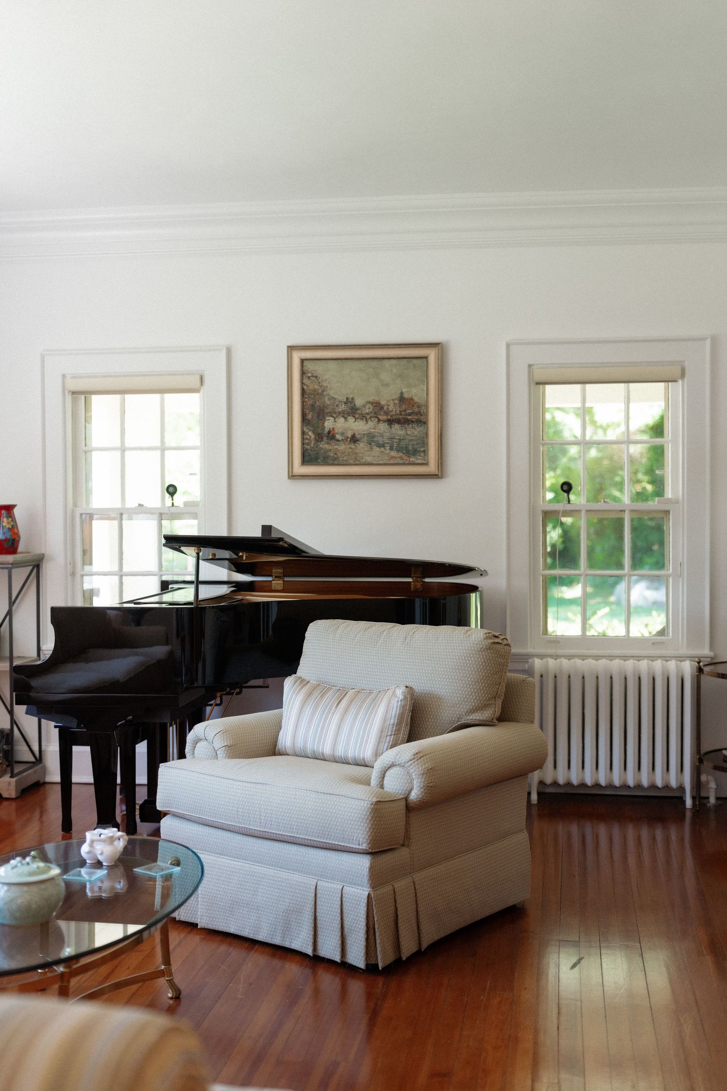 Classic living room with black grand piano, upholstered armchair, hardwood floors, and bright windows.