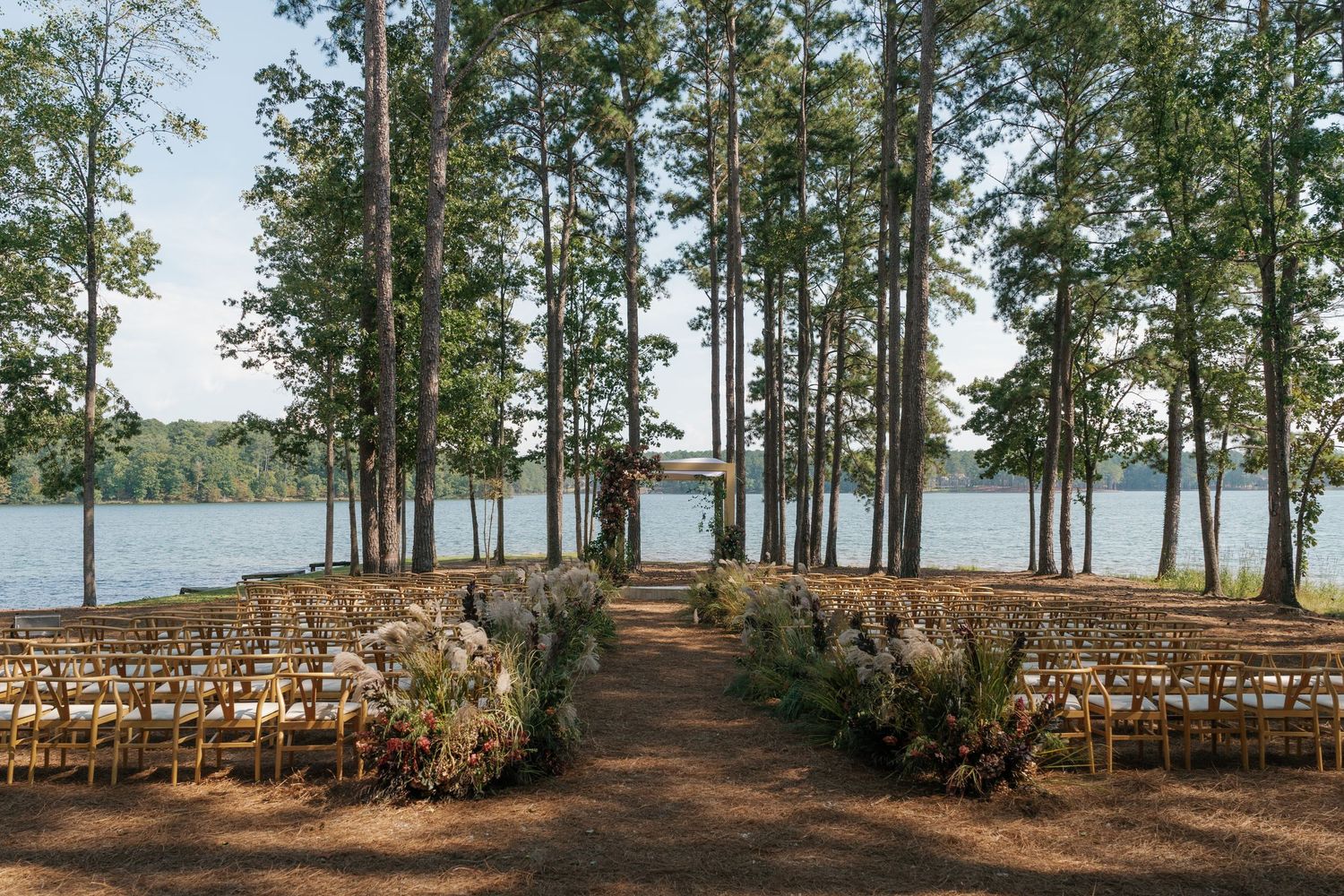 Rustic outdoor wedding ceremony setup with wooden chairs arranged in rows overlooking a serene lake.