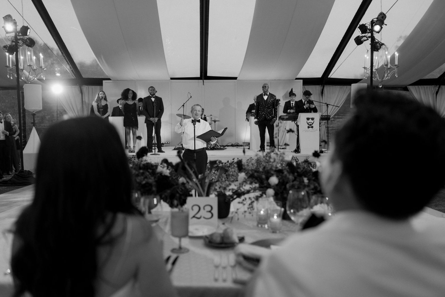 A wide-angle view of a wedding reception with guests dancing under decorative lighting.