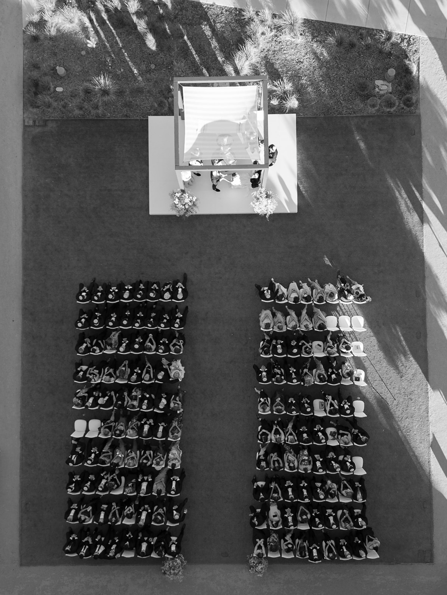 Overhead drone shot of wedding guests arranged in geometric patterns on lawn.
