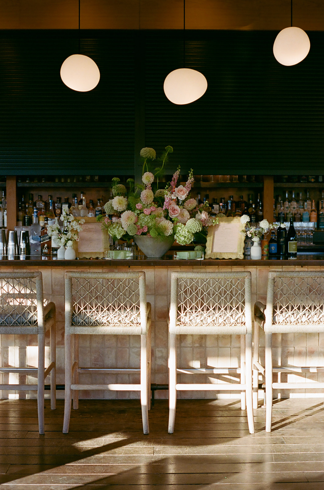 Elegant bar setup with white floral arrangements and modern pendant lights above wooden barstools.