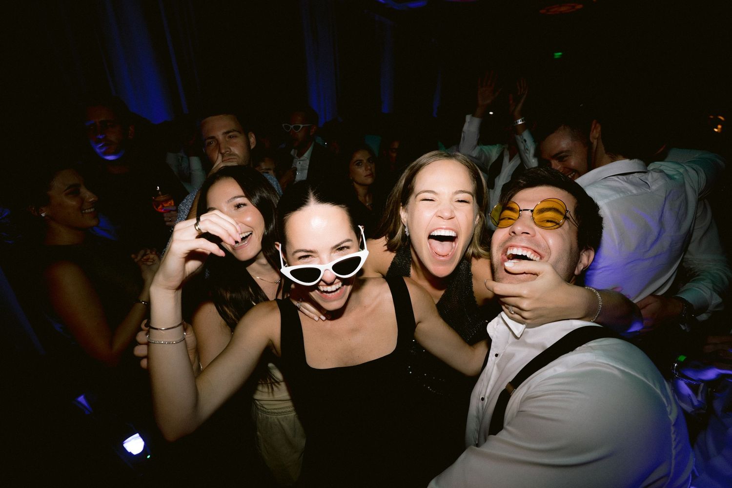 Candid party shots of wedding guests dancing under colorful lighting effects.