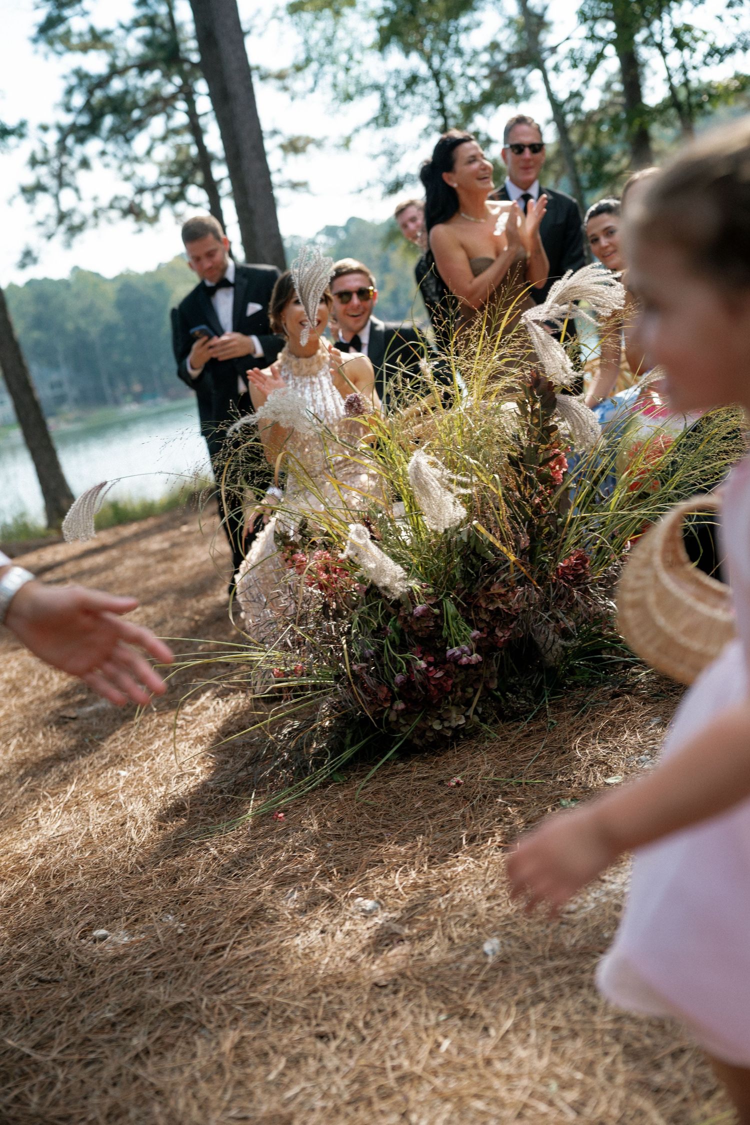 Wedding guests seated outdoors among pine trees with decorative floral arrangements.