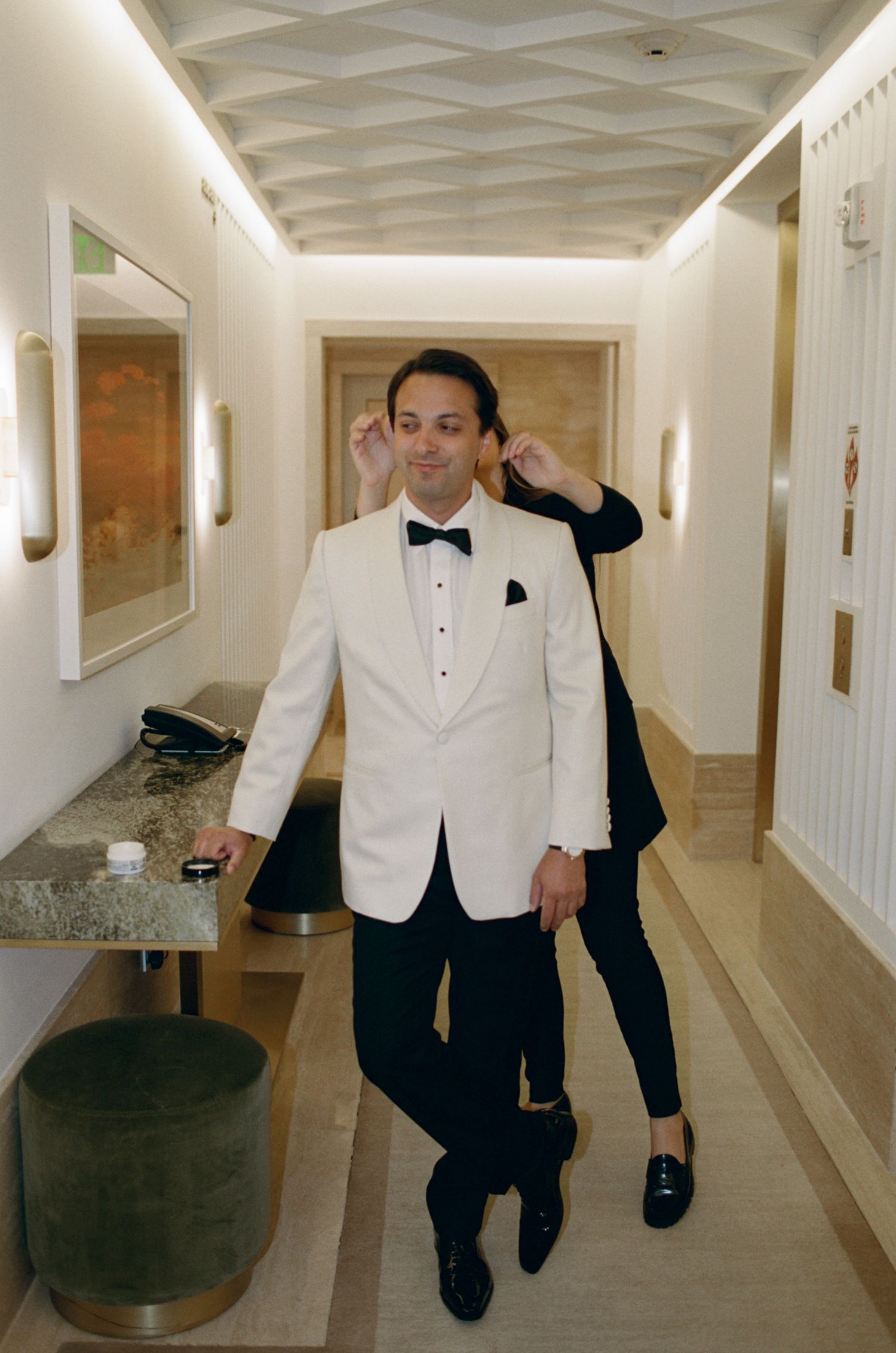 Person in white tuxedo jacket walking through an elegant hotel hallway.
