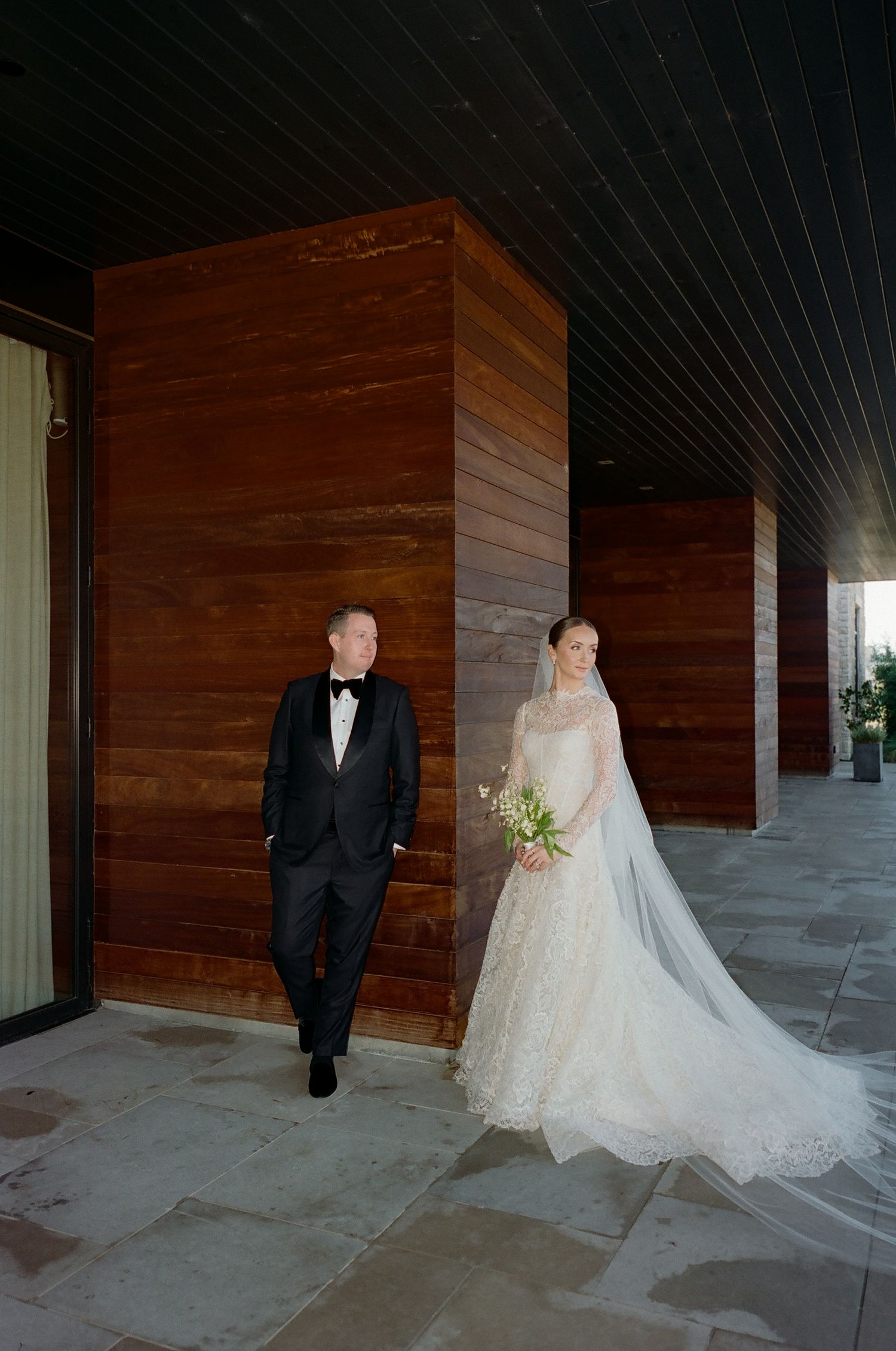 Wedding couple posing against wooden paneled walls in formal attire.