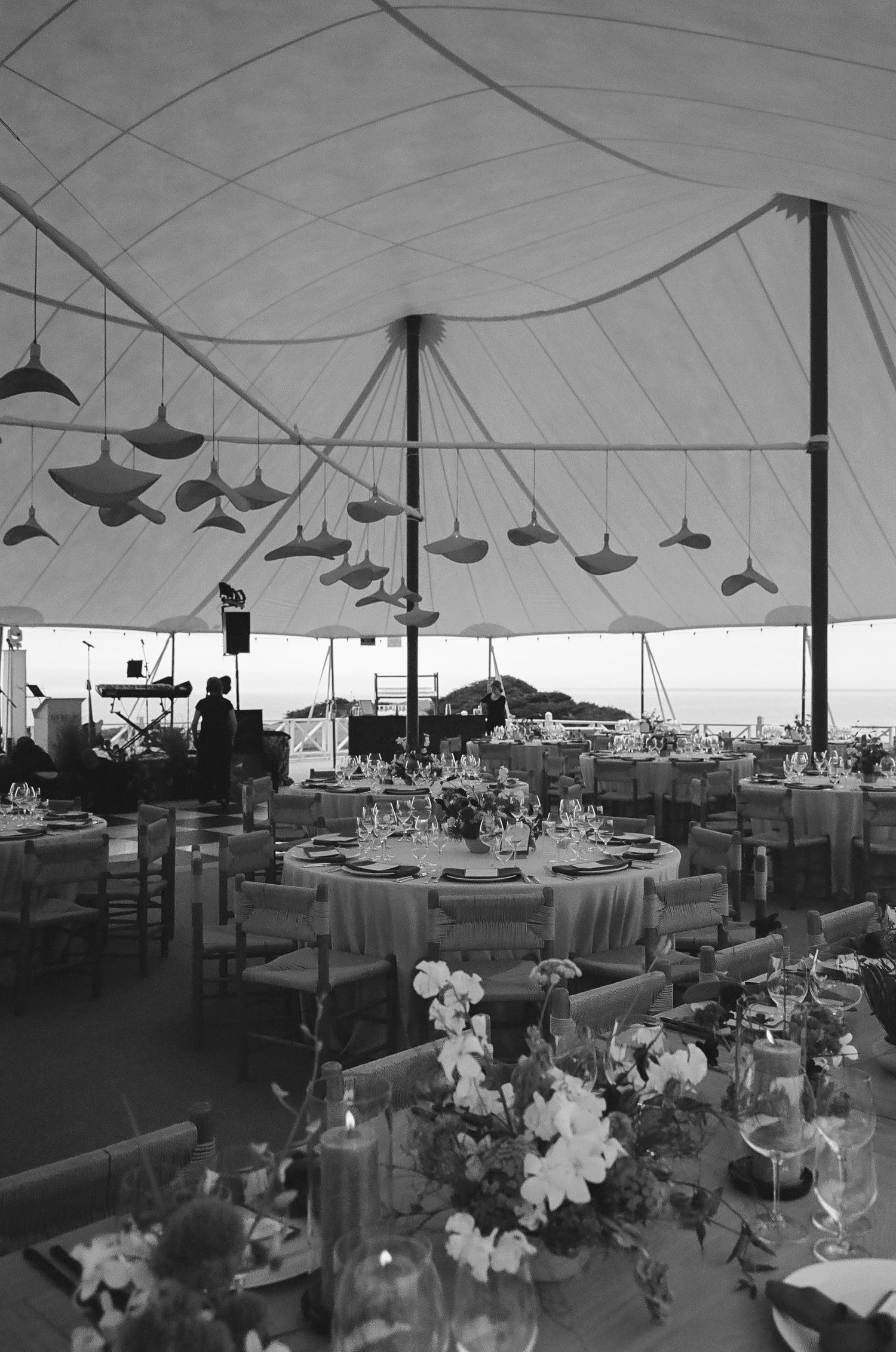 Large white wedding tent interior with tables set for reception and hanging pendant lights.