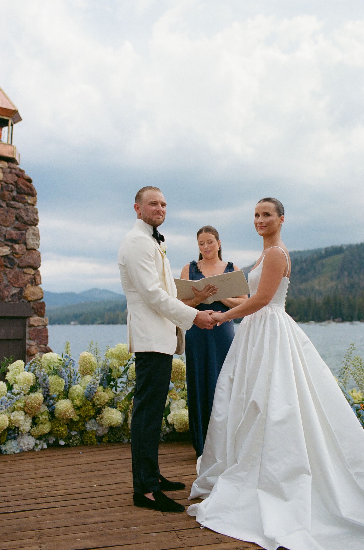 Wedding ceremony takes place on a lakeside deck with mountain views and floral arrangements.