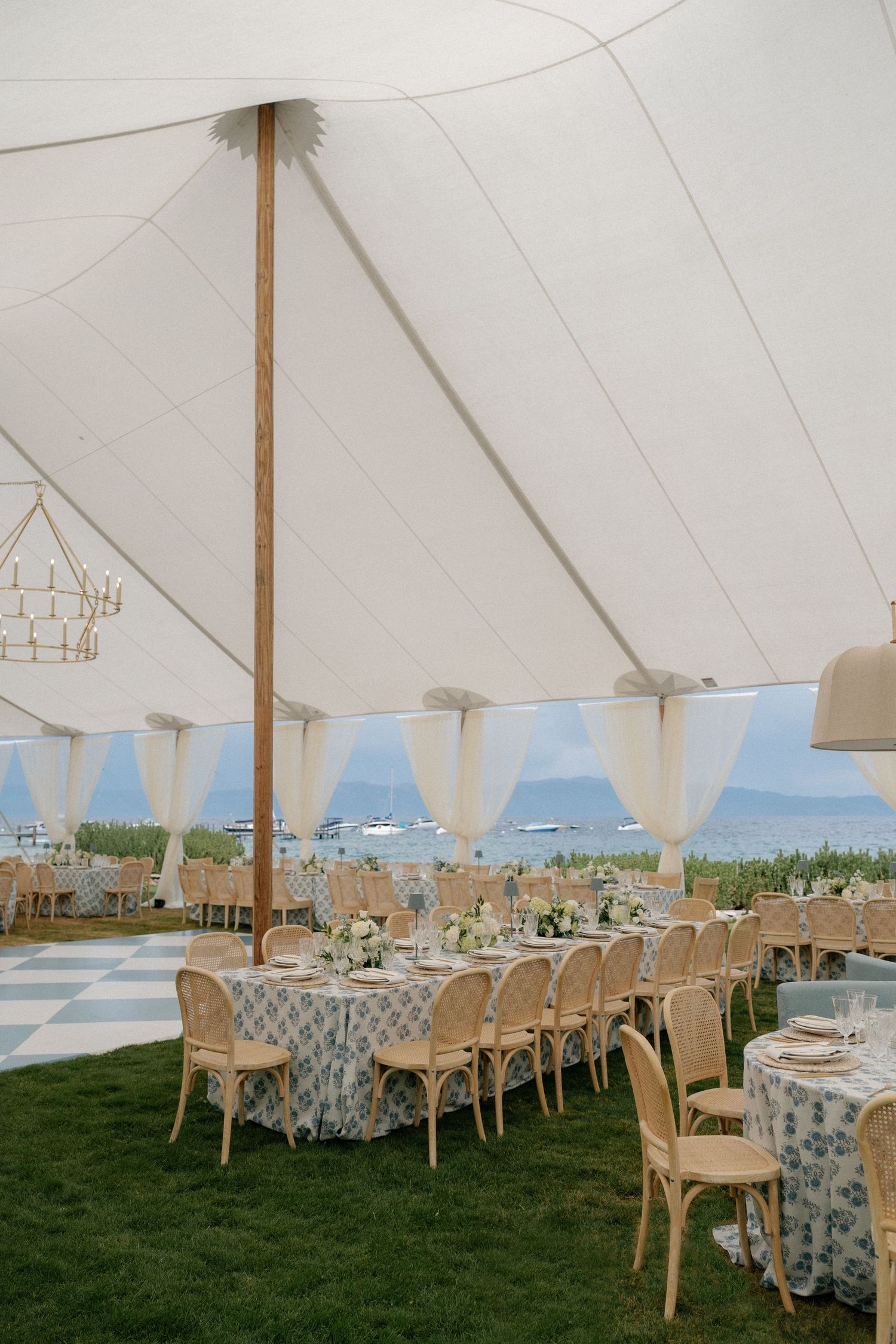 White wedding tent interior with elegant table settings and blue floral linens on a grassy lawn.
