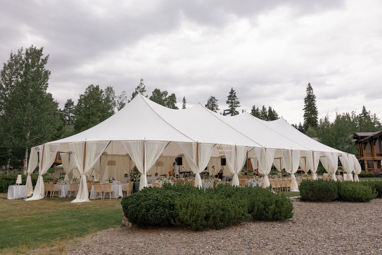 Row of pristine white wedding tents set up on grassy grounds with trees in the background.