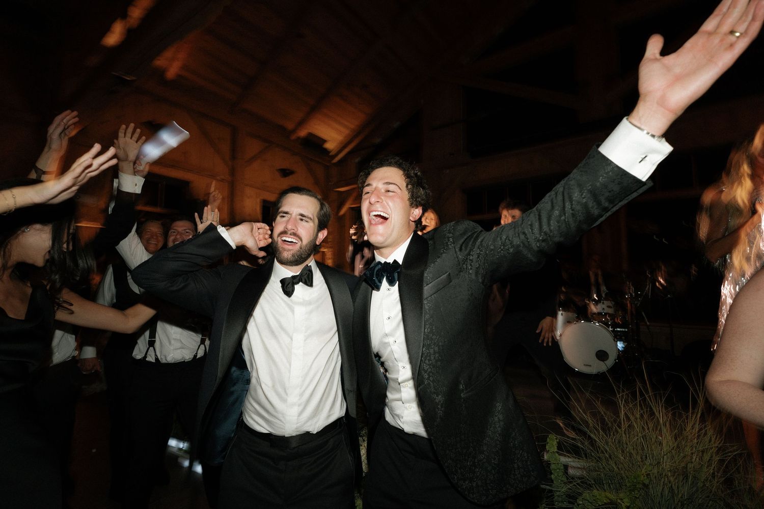 Wedding reception guests dancing with arms raised in celebration.